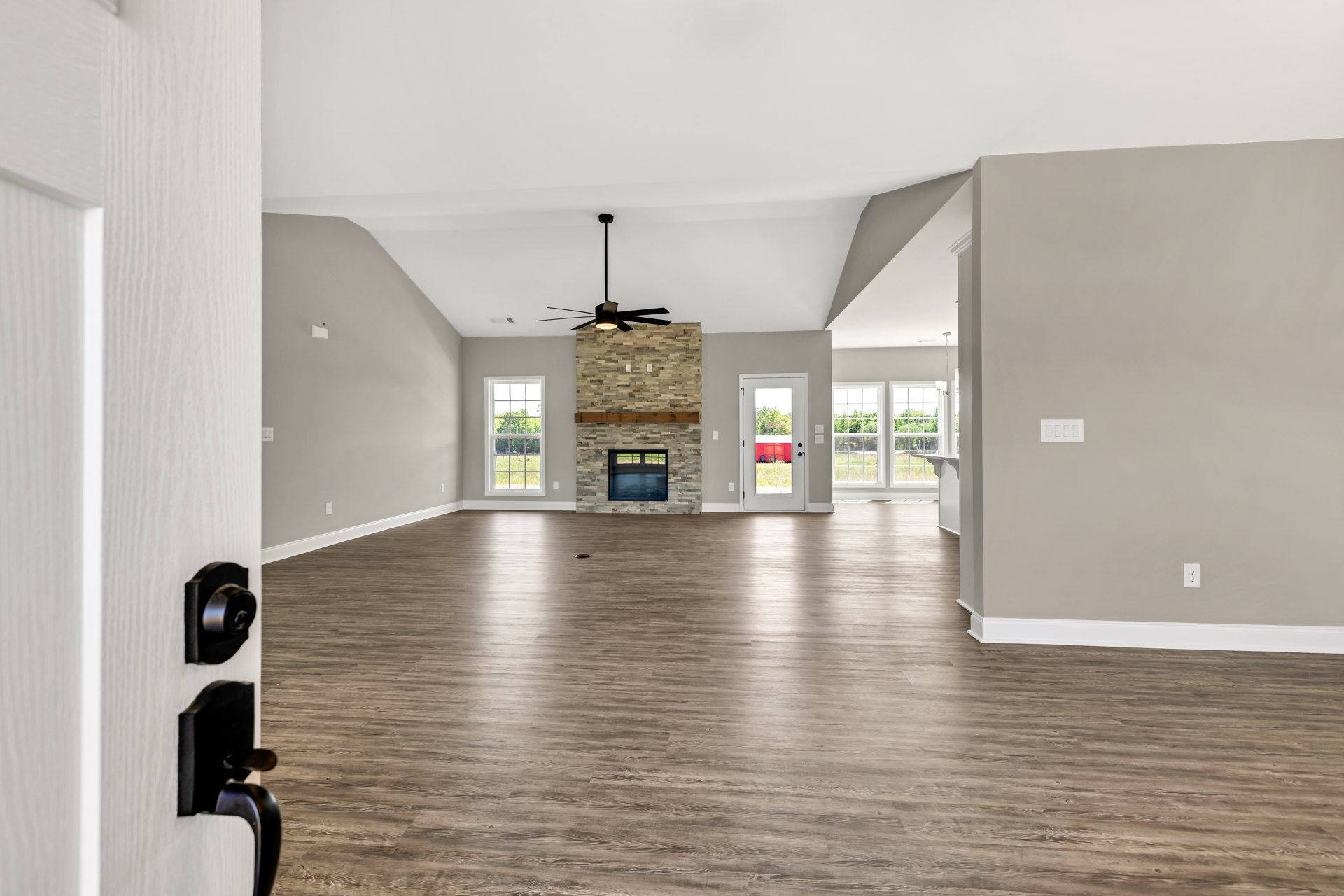 Spacious living room featuring hardwood floors, plaster walls, wood fireplace with mantle, large windows overlooking trees, glass-paneled door, and brick accent wall.