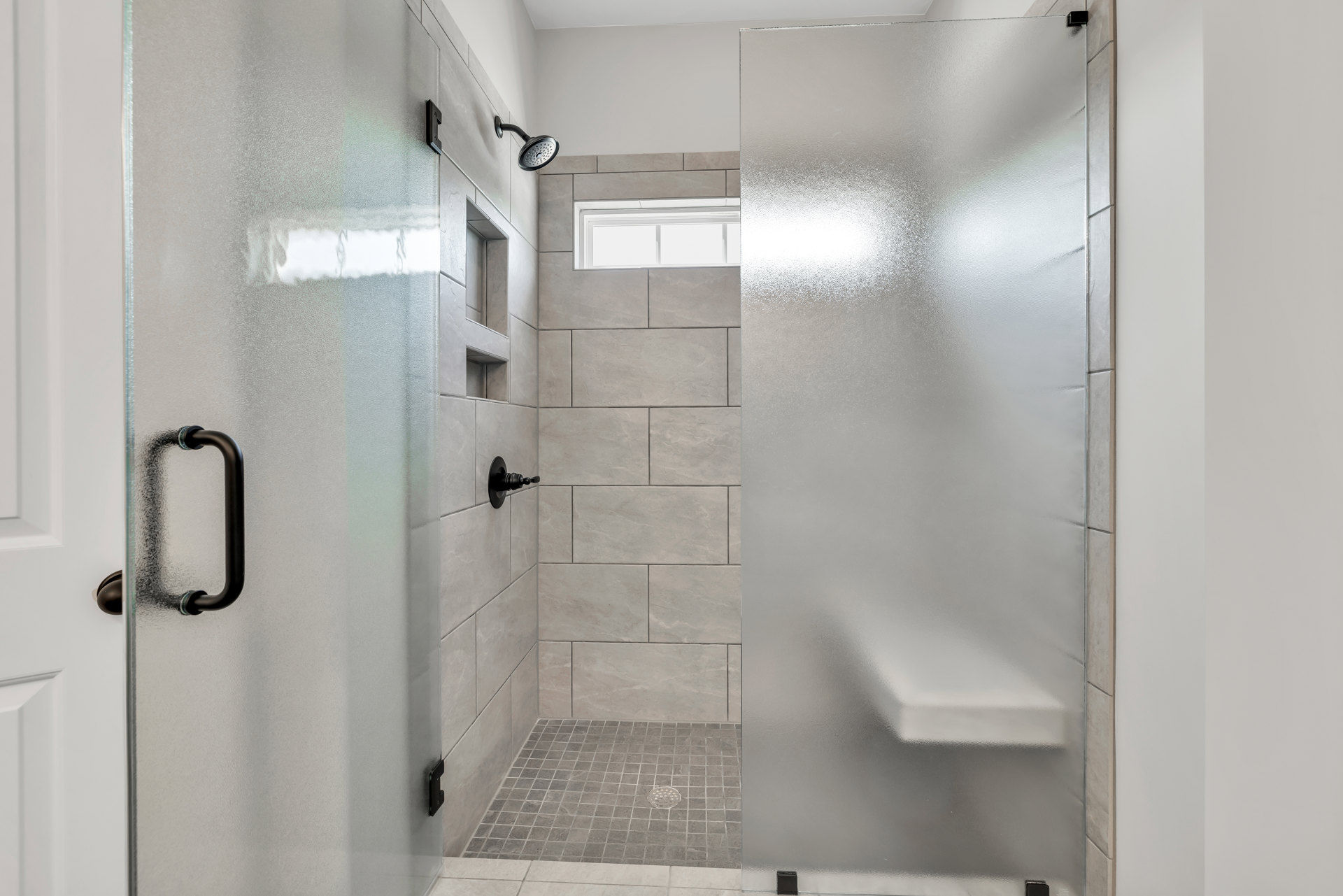 Shower with frosted glass doors, black metal hardware, silver shower head, and light tile walls