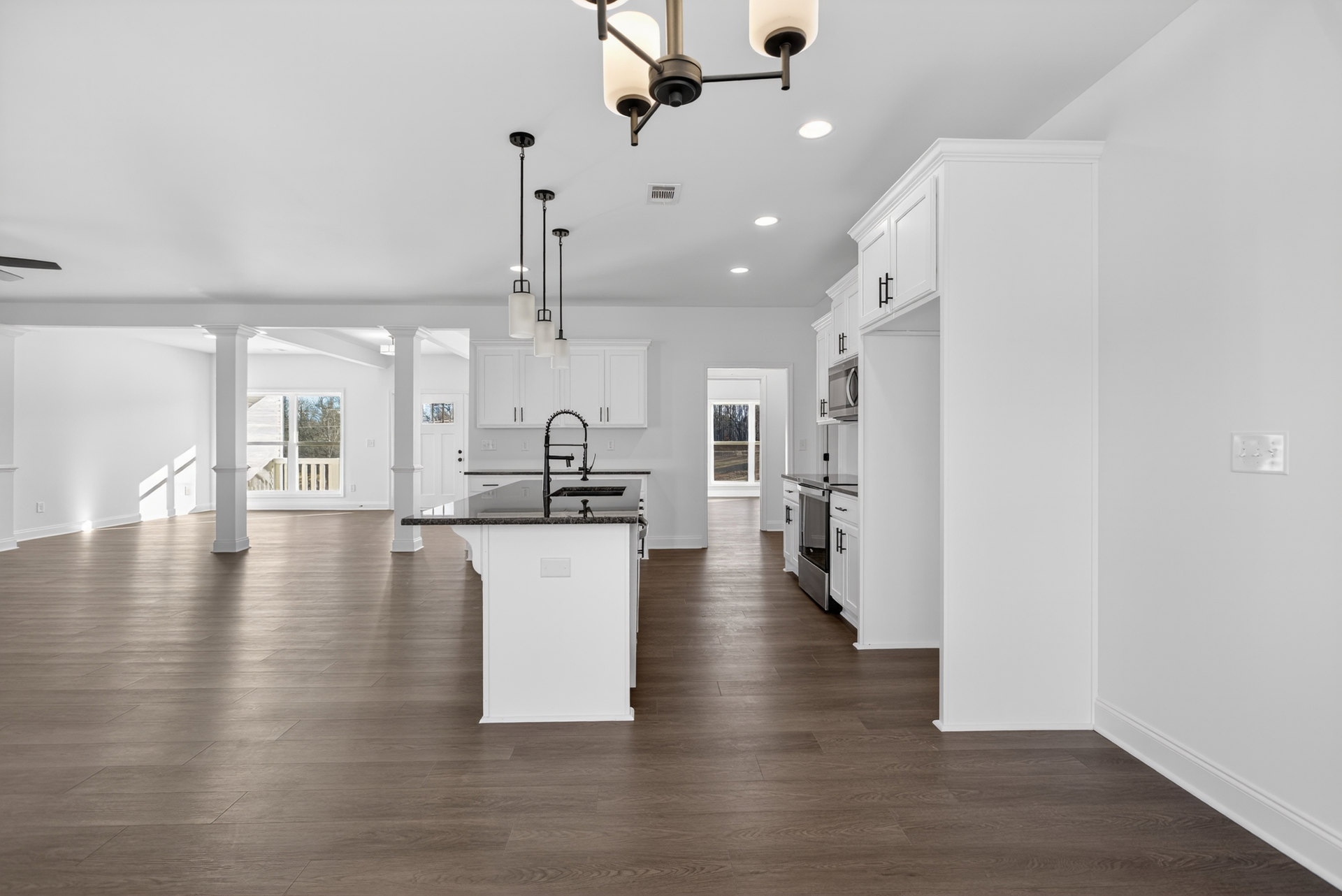 Kitchen and dining area featuring white cabinets, black countertops, wood flooring, white walls, and modern track lighting fixtures.