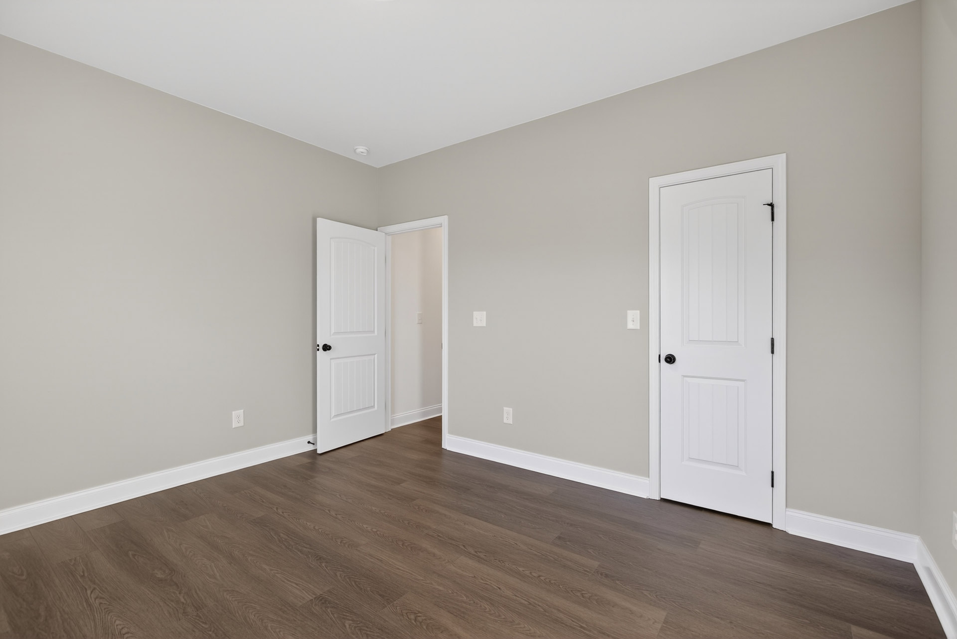 White doors with black knobs, dark hardwood floor, white baseboards, light grey walls, white ceiling, visible light switch on wall