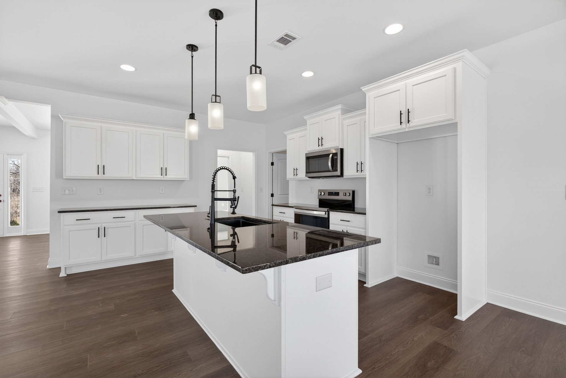 Modern kitchen featuring black stone countertops, white cabinetry, stainless steel microwave, central island with integrated sink, and light wood flooring