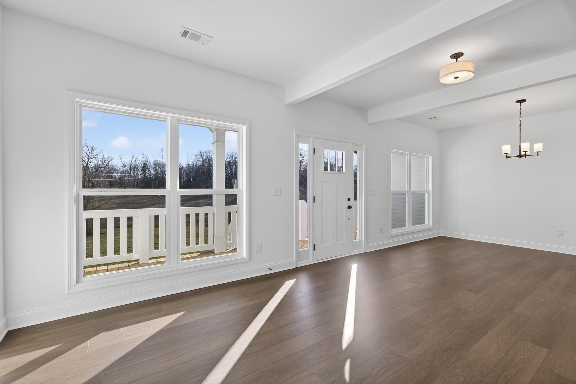 Wood flooring and white walls in a bright room with a white door, window with white railing, and ceiling light fixture with a white shade