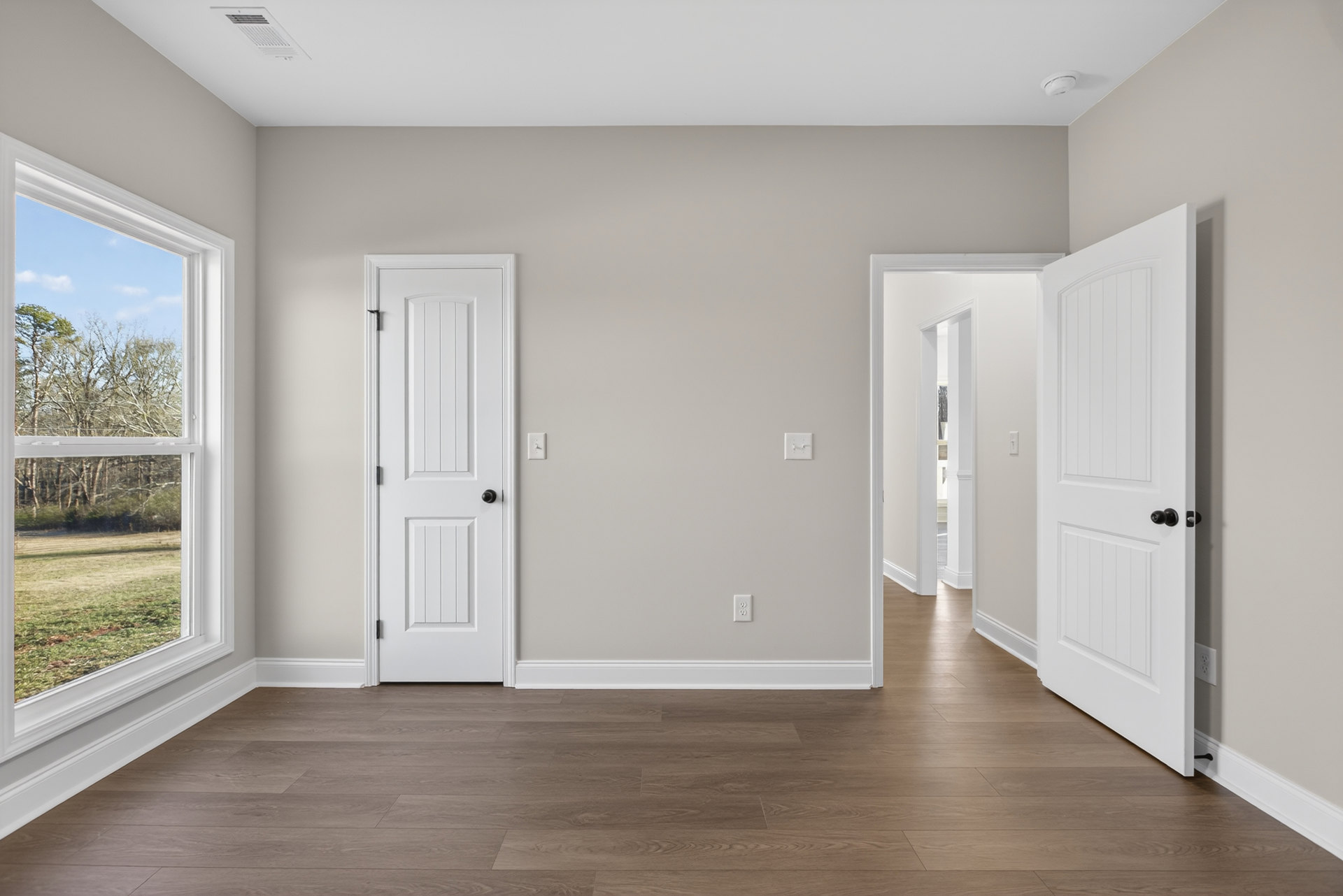 Wood floor with white baseboards, white doors featuring black knobs, window overlooking trees