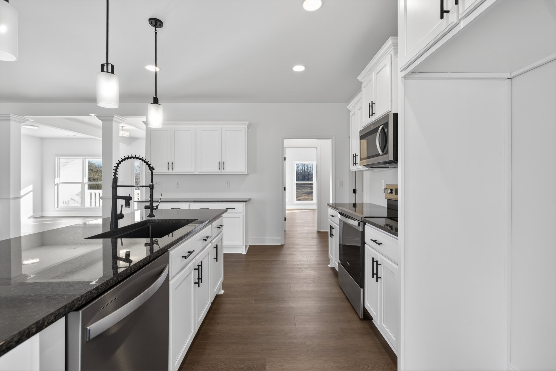 White kitchen cabinets, black appliances, wood flooring, black countertop, stainless steel sink, built-in microwave, neutral wall color