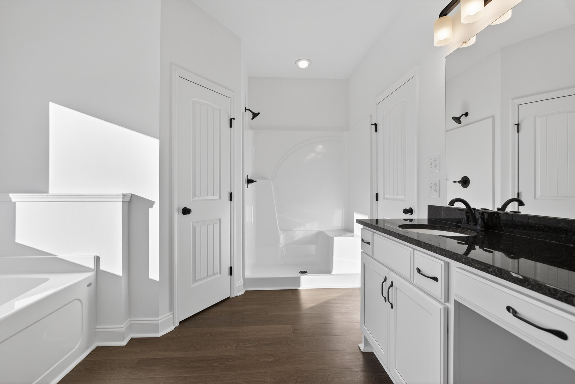Bathroom with white walls, wood flooring, freestanding white bathtub, white vanity sink, and white door with black handle