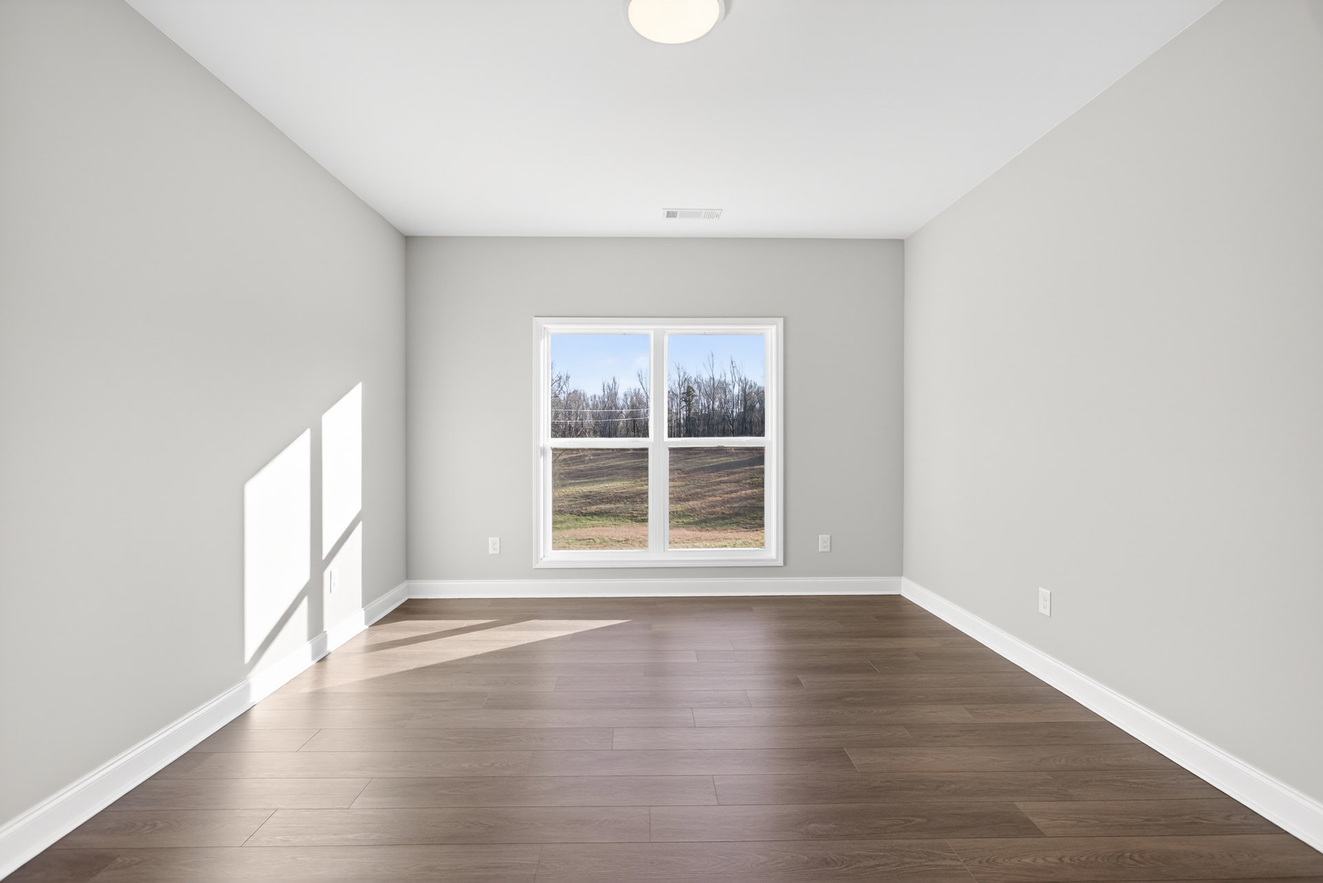Hardwood floor room with white walls, large window overlooking field and trees, simple baseboard molding