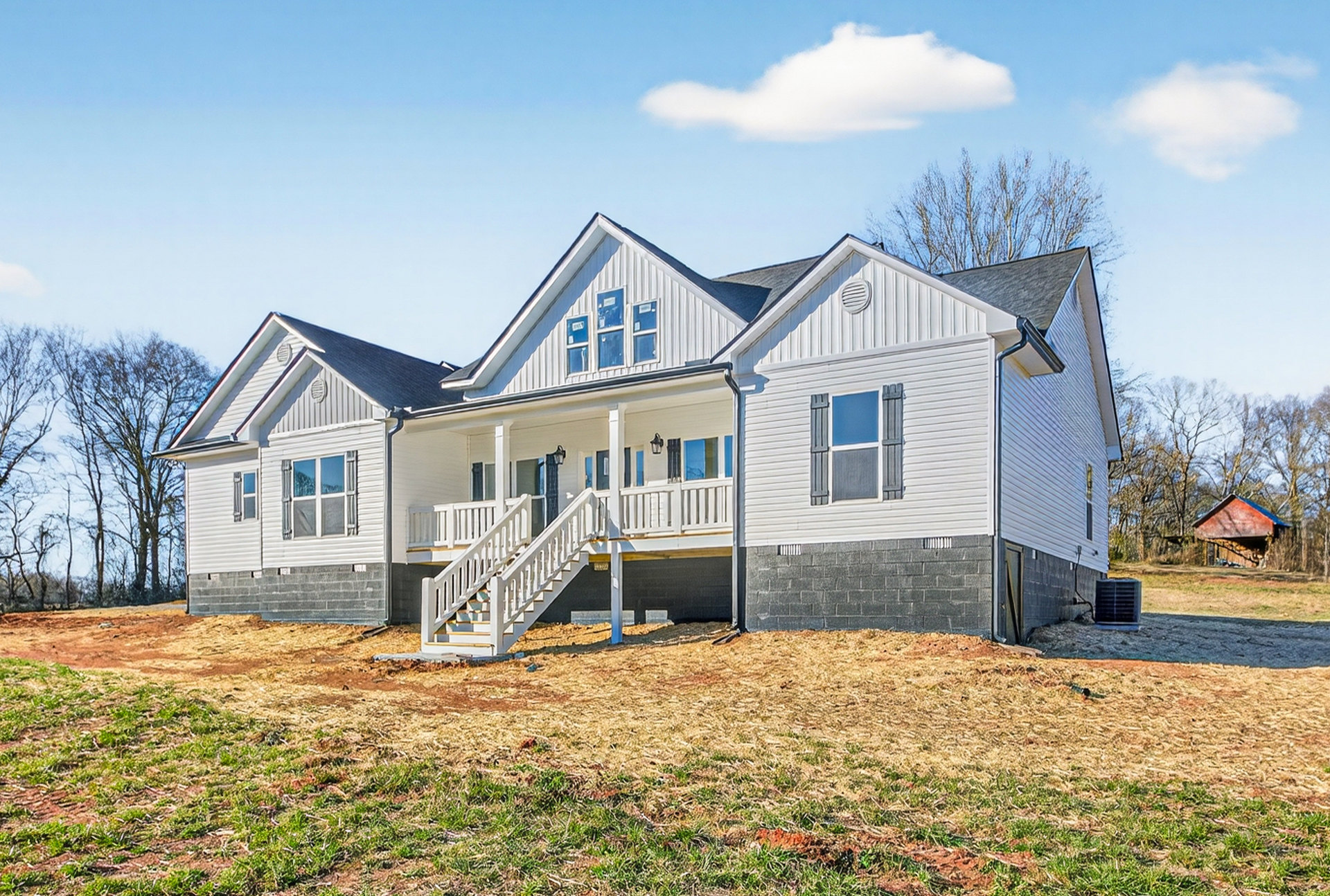 Two-story house with white siding, covered front porch, wooden stairs, large windows, manicured lawn, and blue sky with scattered clouds
