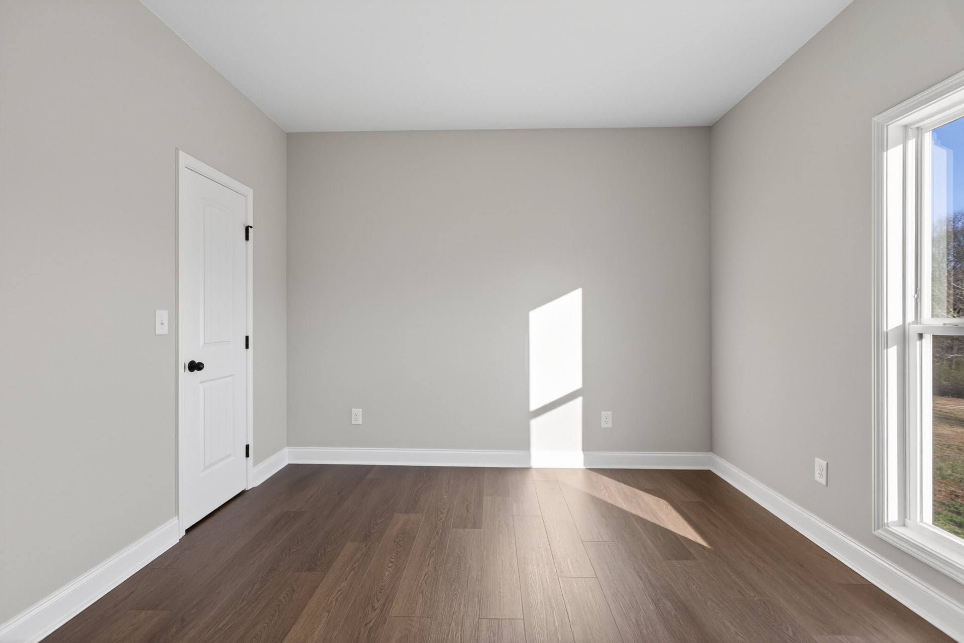 Wood floor with white trim, white door with black knob, window with white frame, sunlight casting window shadow on white plaster wall