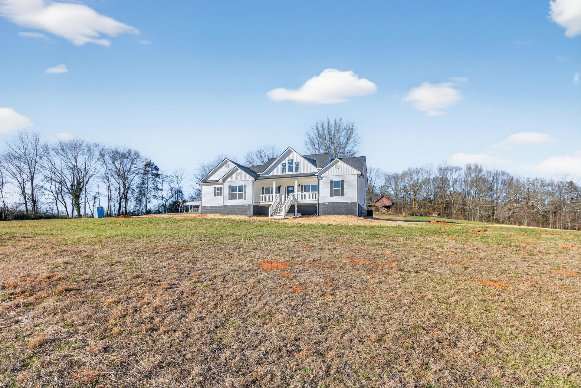 Two-story house with large white roof, front porch, and white exterior stairs, set on a spacious grassy hill under a partly cloudy sky