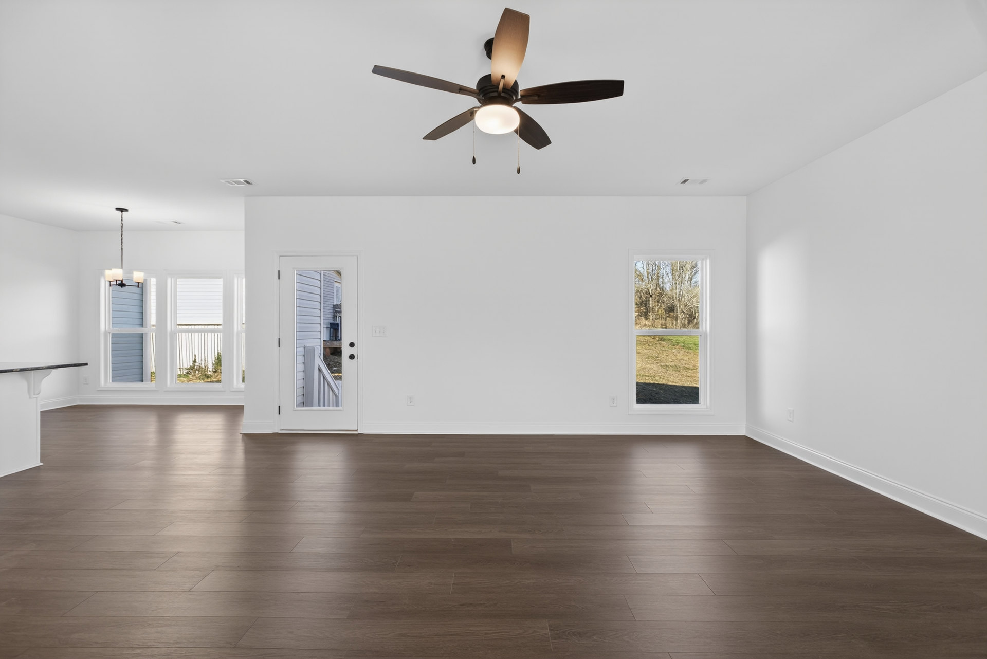 Ceiling fan with light fixture above wood laminate flooring, white walls, large window overlooking forested landscape