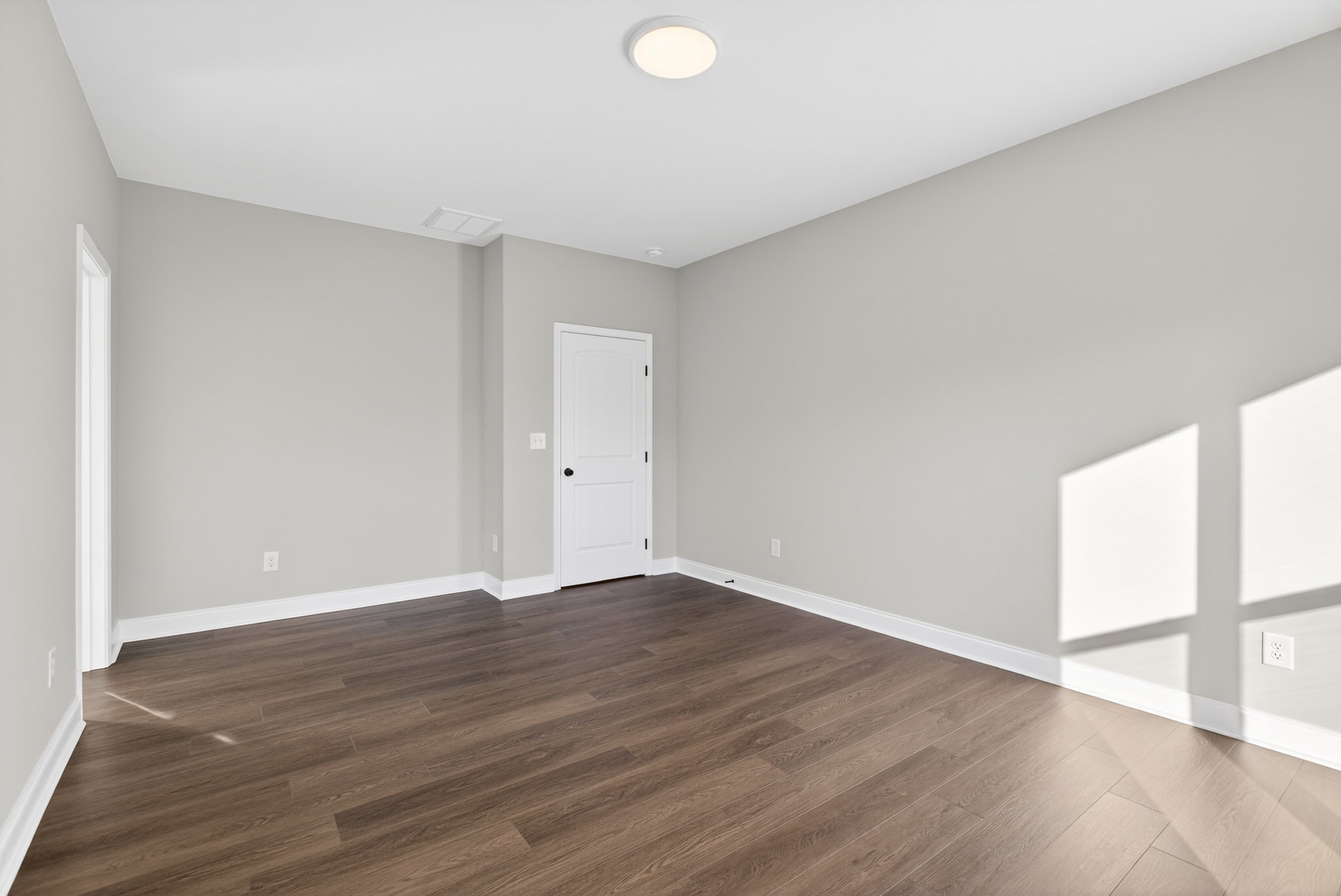 Wood flooring and white walls with a white door featuring a black knob, illuminated by a ceiling light.