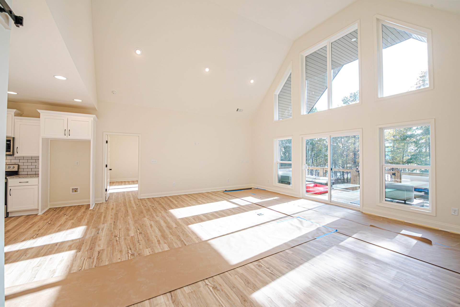 Spacious room with hardwood flooring, large windows, white cabinetry with black handles, and built-in microwave oven