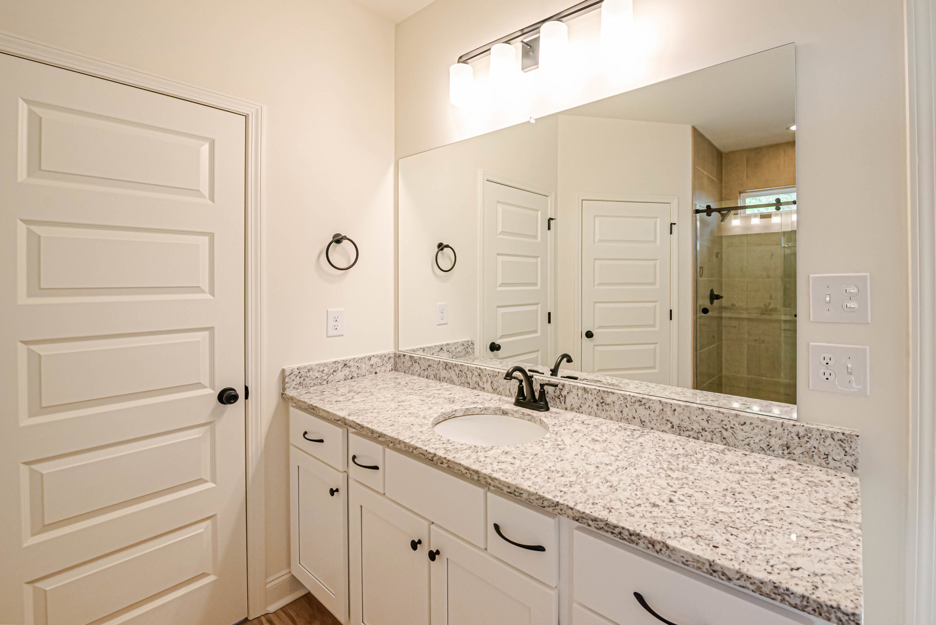 Bathroom featuring a marble countertop with a circular white sink, black metal towel holder, large mirror above the vanity, white door with black knob, and dual light switches on a