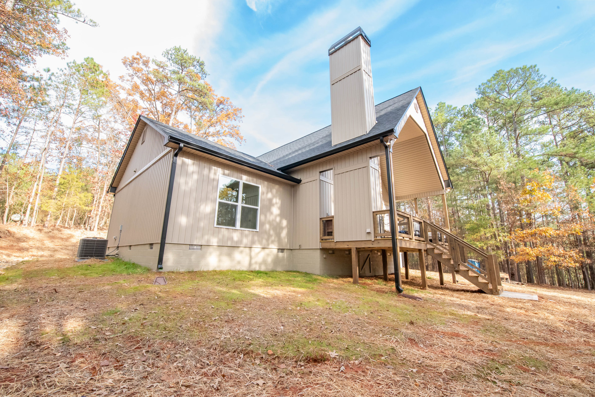 Two-story home with brick chimney, wood deck, large windows reflecting nearby trees, attached garage, and front porch with stairs