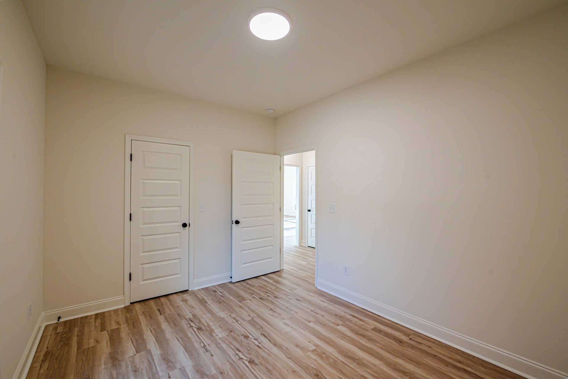 Hardwood floor with white paneled doors featuring black knobs, white walls, and recessed ceiling light