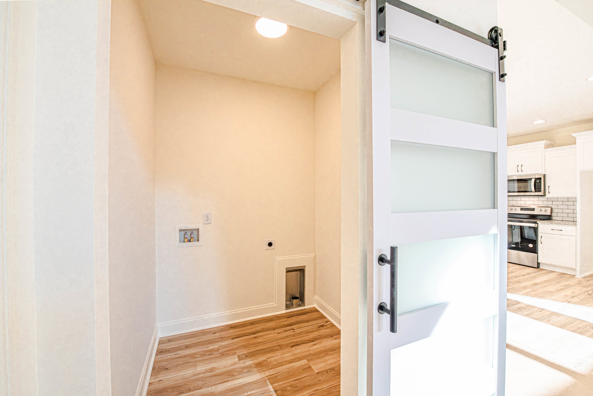 White door with black handle, wood flooring, white walls, recessed ceiling light, partial view of cabinetry and sliding door