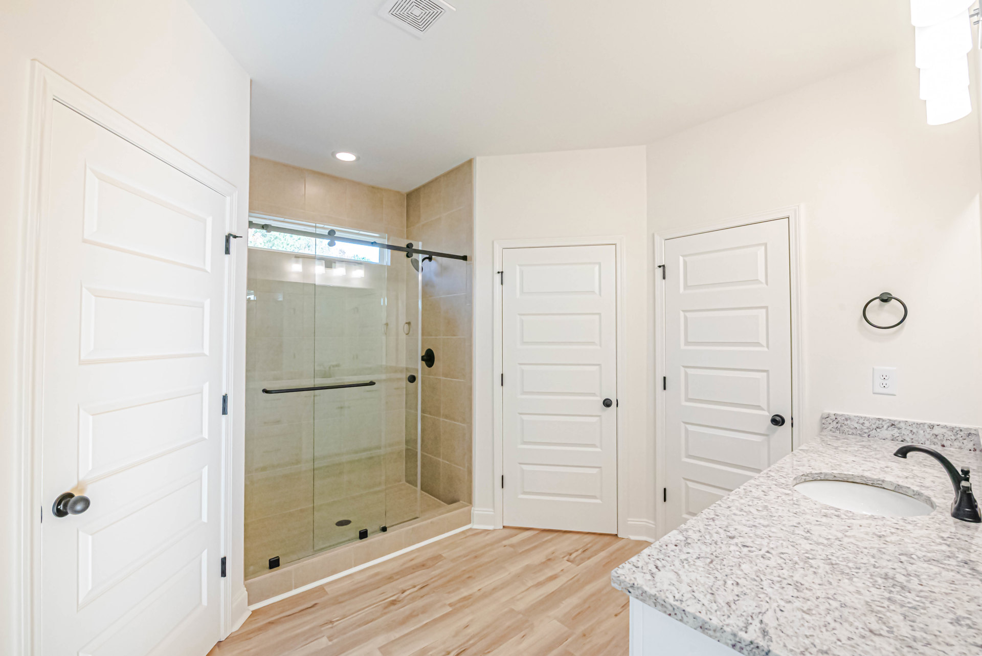 Bathroom featuring a frameless glass shower with black hardware, white marble countertop sink, white door with black handle, and light gray tile flooring.