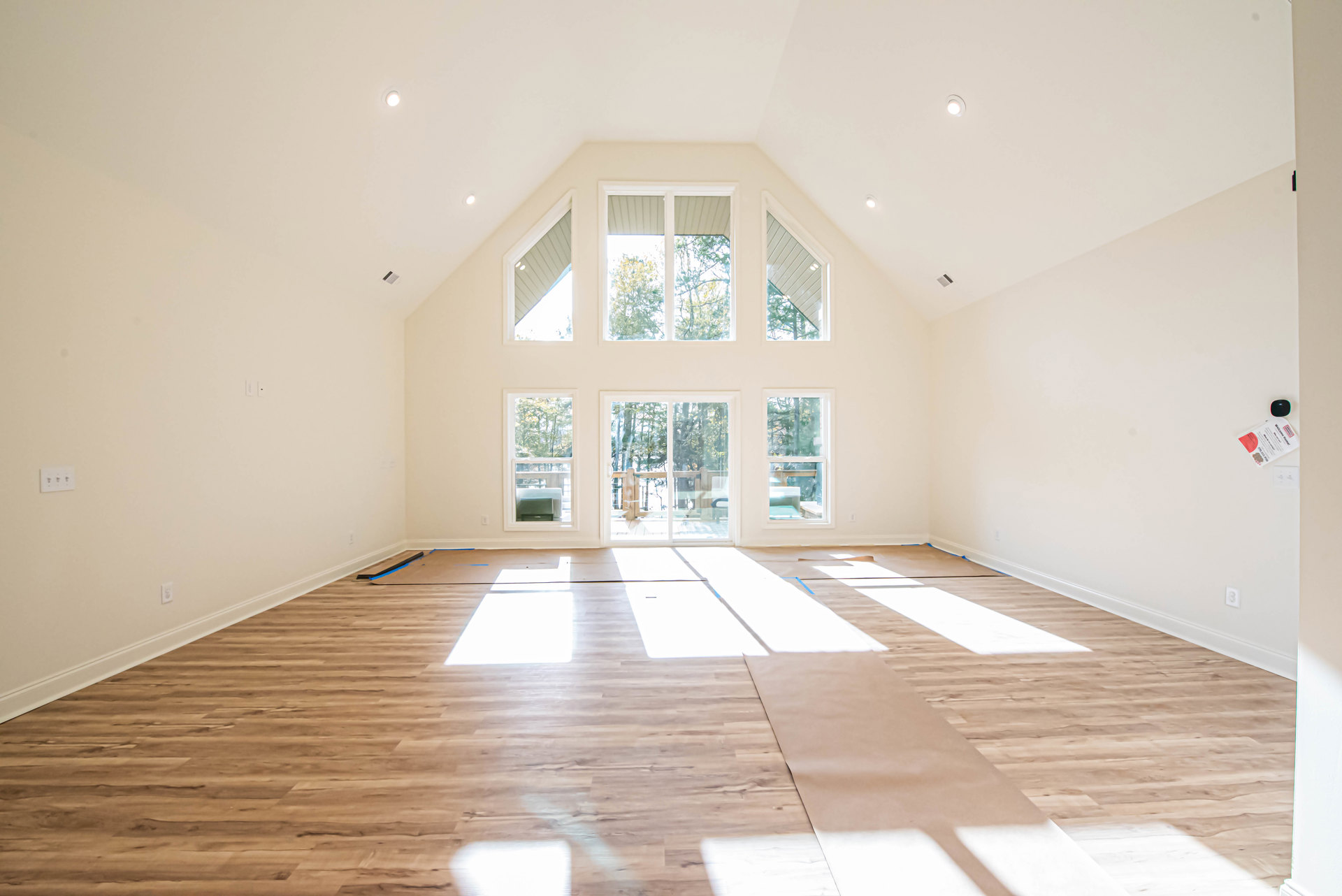 Spacious room featuring wood flooring, large windows with views of trees, white walls, and a ceiling with recessed lighting