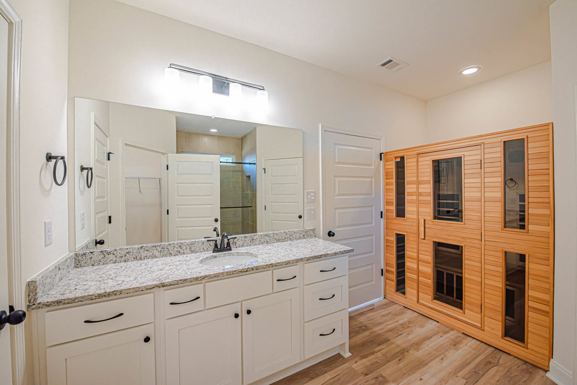 Bathroom featuring a wide mirror above a tile countertop, wooden sauna with glass door, cabinetry, and modern plumbing fixtures