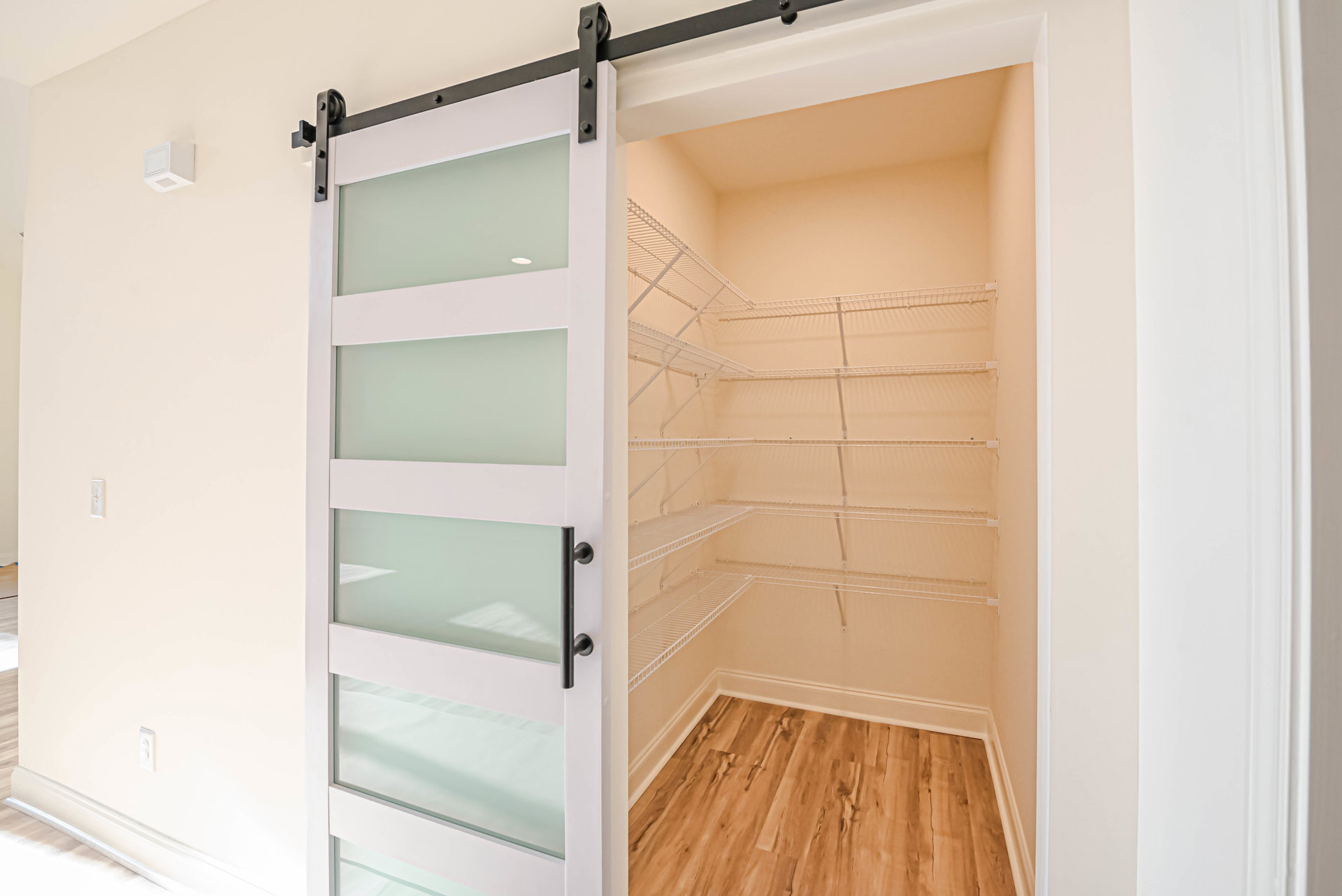 Closet with sliding white doors featuring glass panels, wood flooring with white baseboards, built-in shelves inside closet, white ceiling with black trim, white square vent on