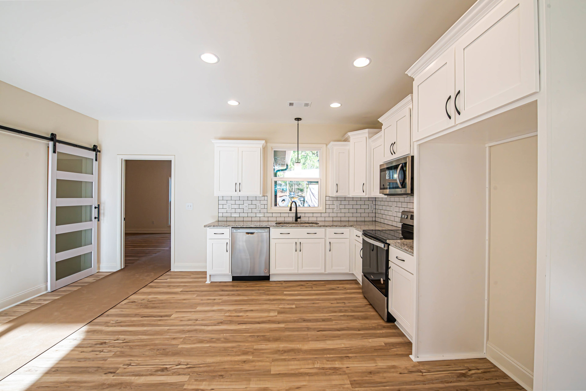 Kitchen with white shaker cabinets, stainless steel appliances, glass-paneled door, hardwood flooring, white walls, and a window letting in natural light