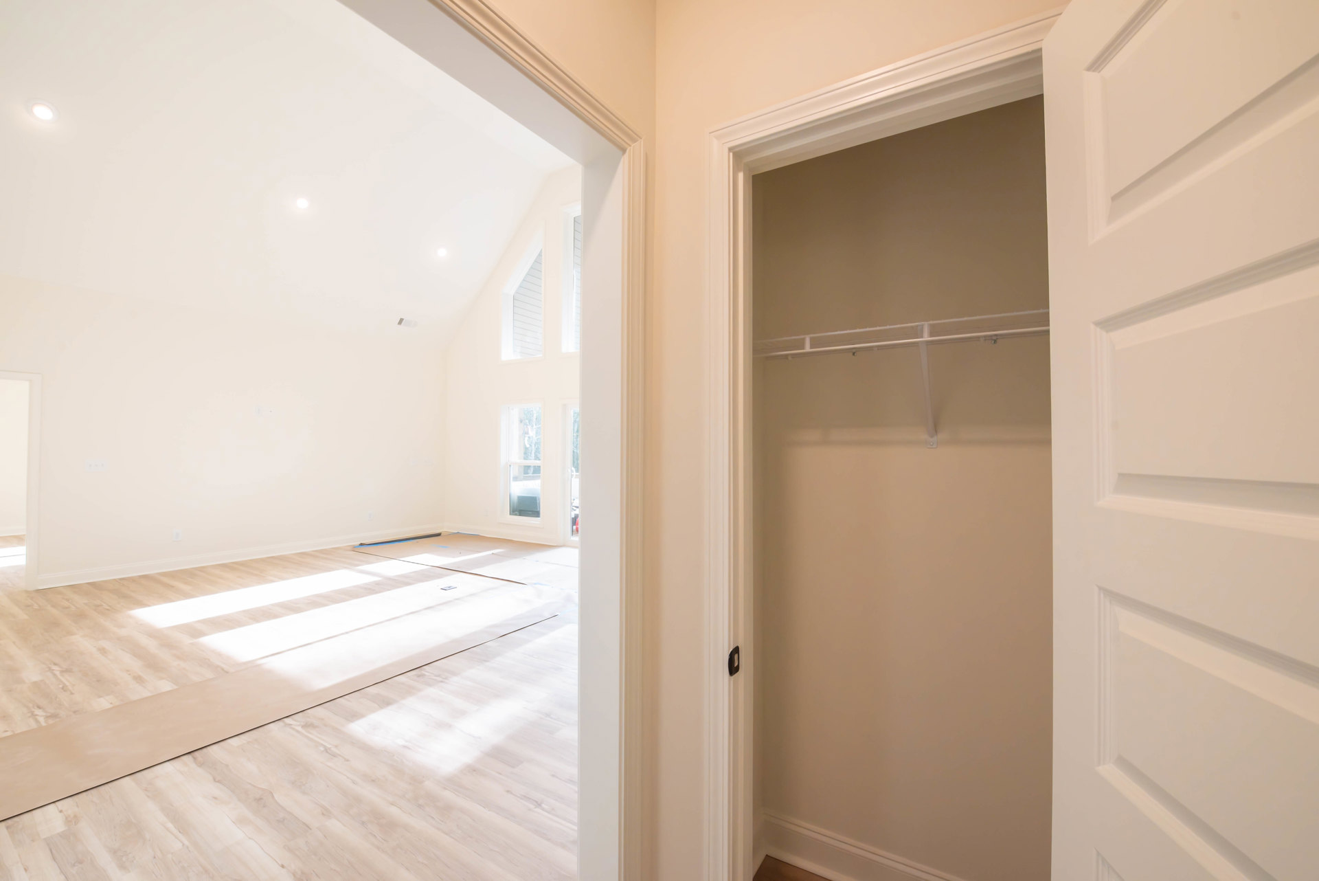 Hardwood floor room with white walls, white closet featuring built-in shelf, square-patterned white door, blue painter’s tape on baseboard