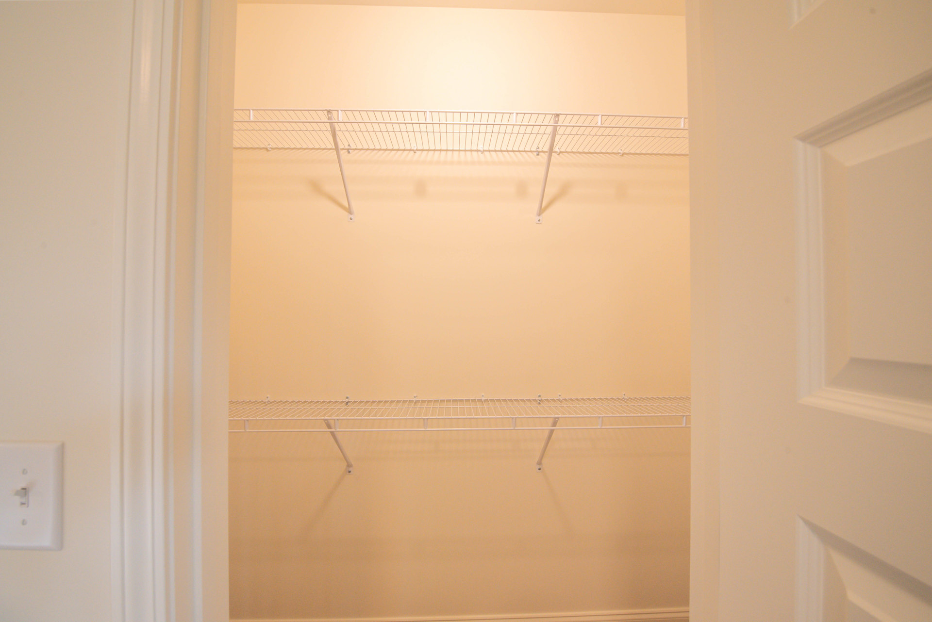 White closet interior with built-in shelves, metal shelf mounted on wall, white door with metal handle, plaster walls and corner detail