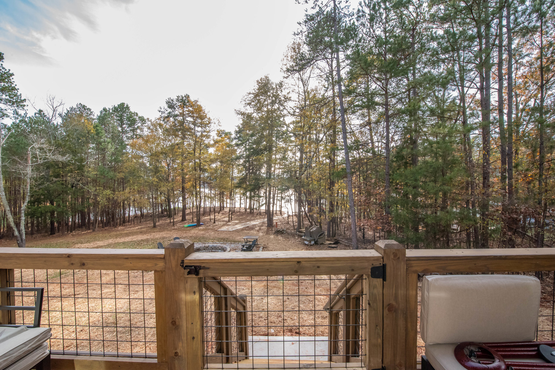 Wooden privacy fence bordering a backyard deck, surrounded by mature trees and shaded outdoor space under a partly cloudy sky