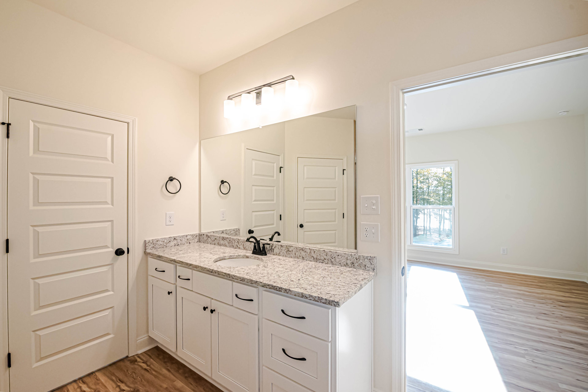 Bathroom featuring a marble countertop with undermount sink, large framed mirror above, black towel holder mounted on white wall, white door with black hardware, wood flooring