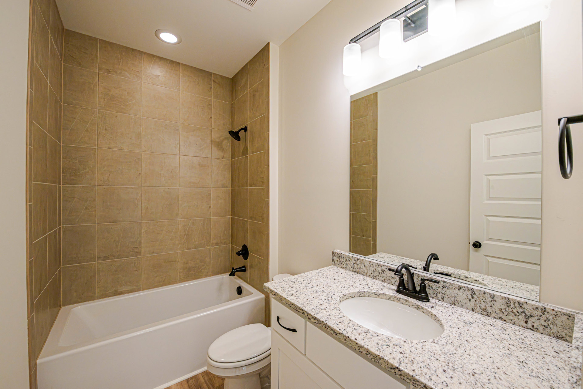 Bathroom with white freestanding bathtub, white sink featuring black faucet, wall-mounted mirror above sink, tile shower wall with chrome shower head, and closed white toilet.