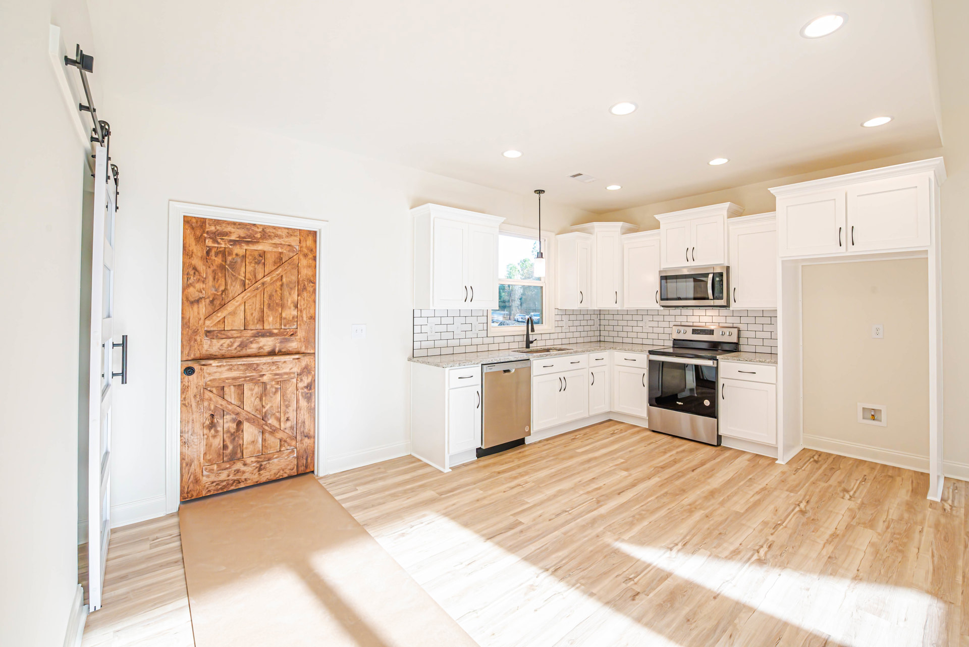 White shaker cabinets, stainless steel appliances, wood plank flooring, stone countertops, and a wooden door with a lock in a modern kitchen.