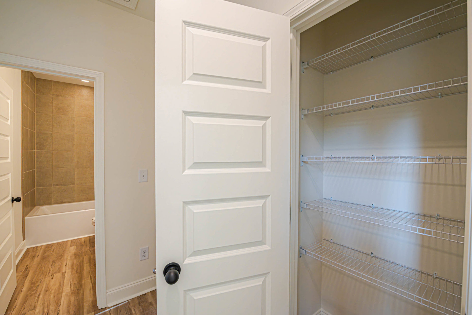 White paneled door with brushed metal knob, surrounded by white walls and built-in wire shelving in a closet.
