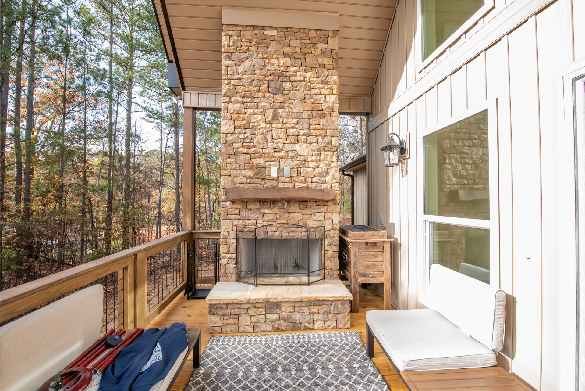 Stone fireplace with screen on a wooden deck, rug on wood floor, red decorative sticks on table, wooden box with faucet, mattress on bed, stone wall backdrop