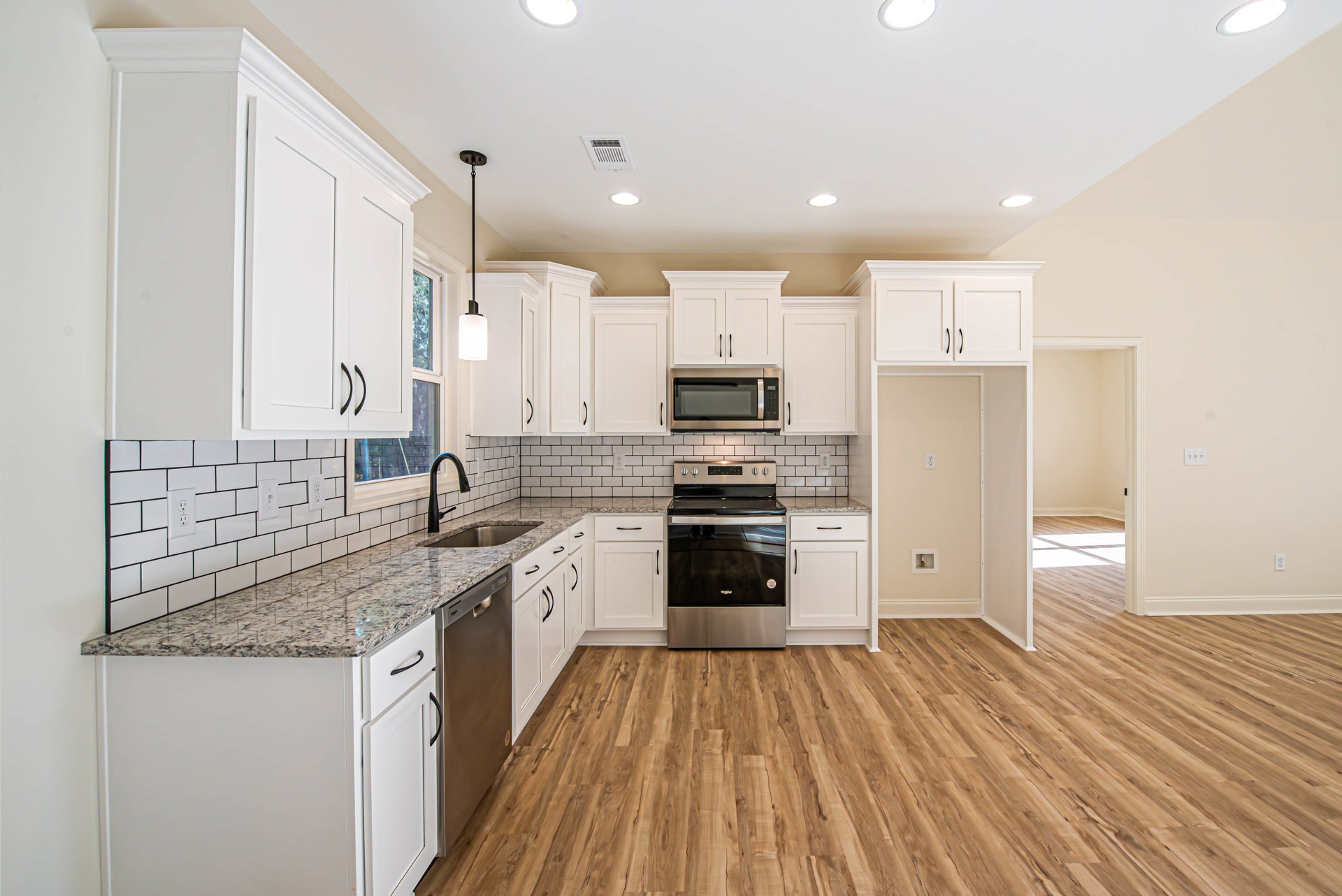 White kitchen cabinets with black handles, wood flooring, black and silver oven, built-in microwave, black faucet on a light countertop