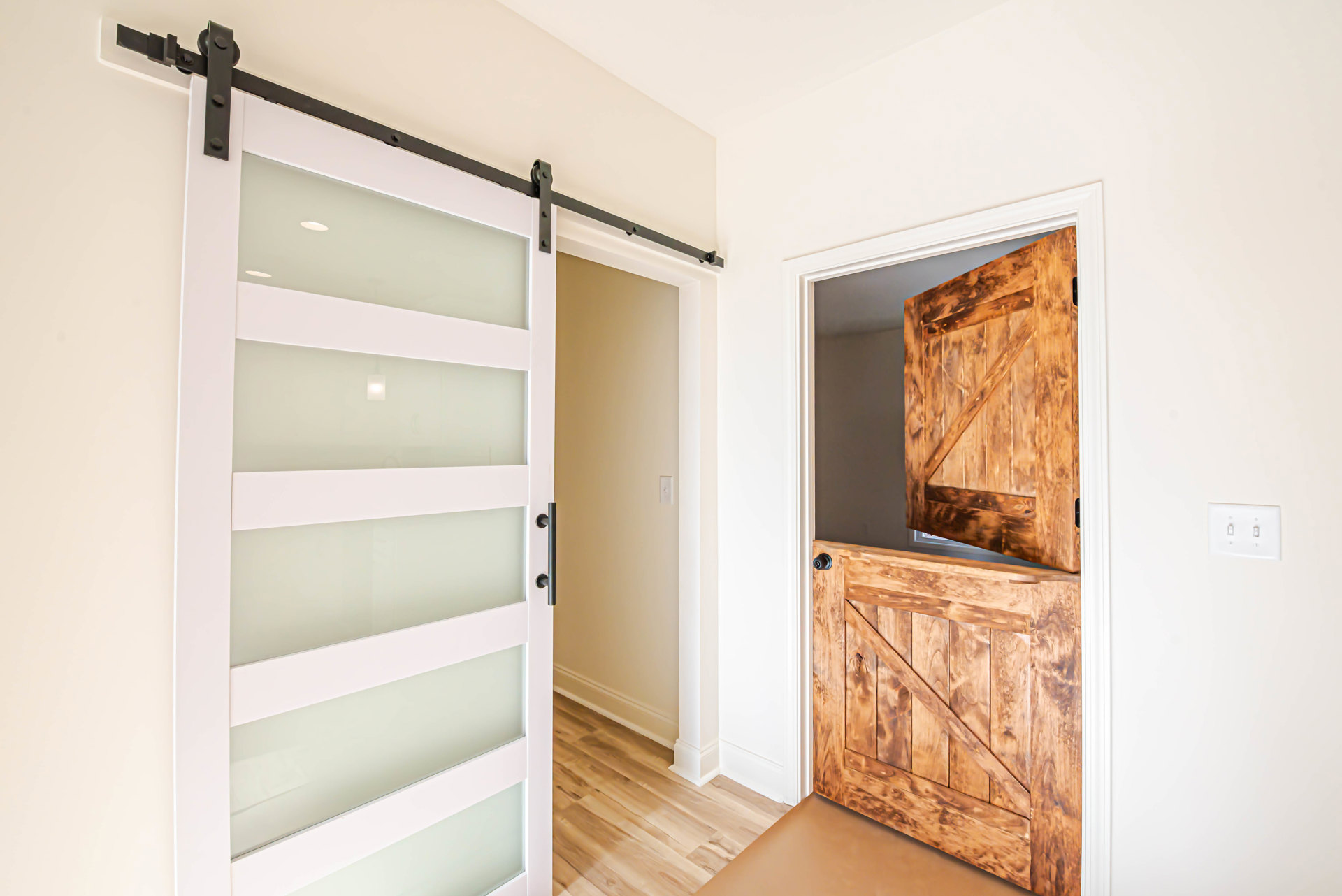 White door with glass panels set in a hardwood wall, light switch nearby, cabinetry and shelving visible in a modern interior room.