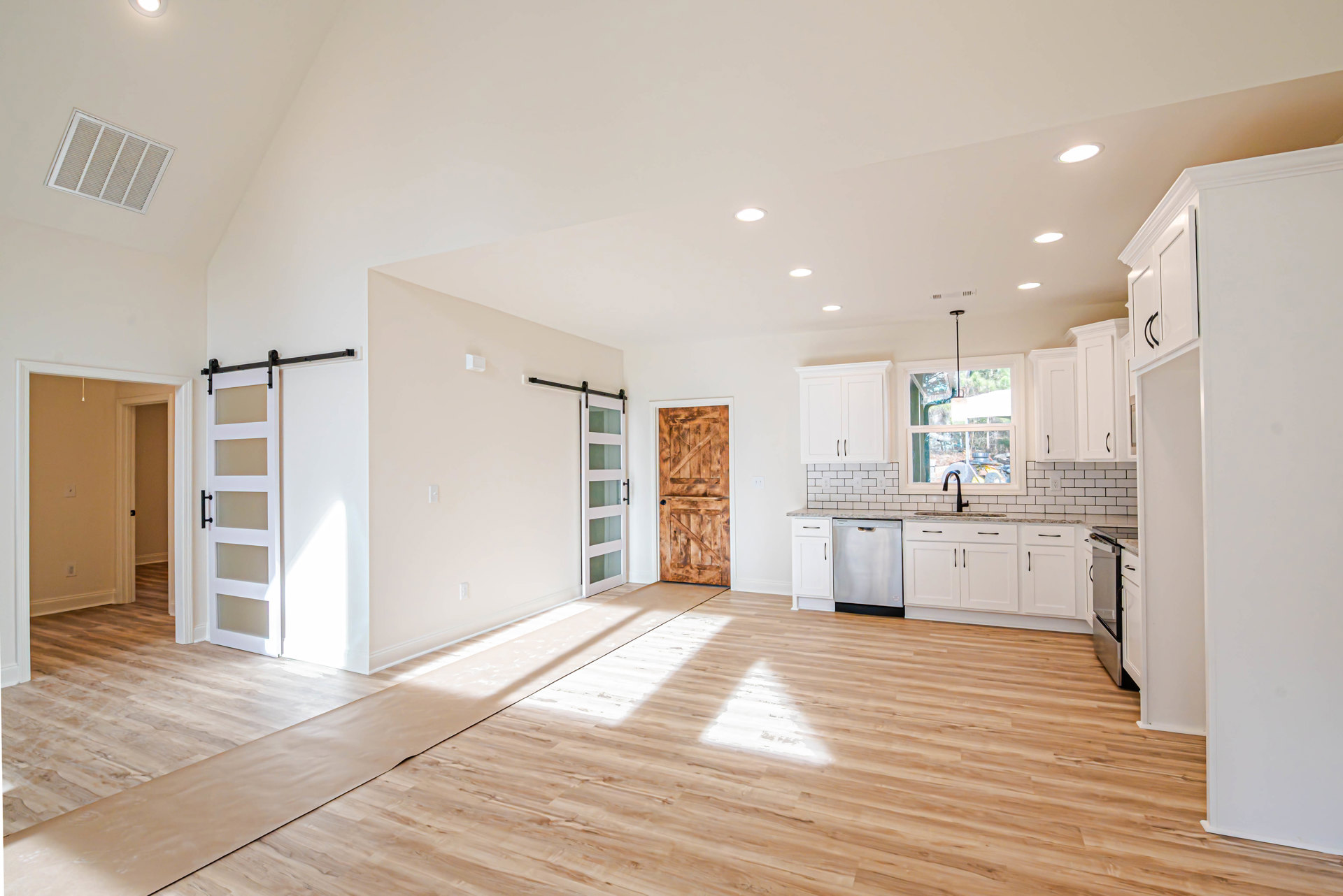 Kitchen with wood flooring, white cabinetry, sliding barn door featuring black hardware, ceiling vent, and adjacent dining area with glass-paneled door