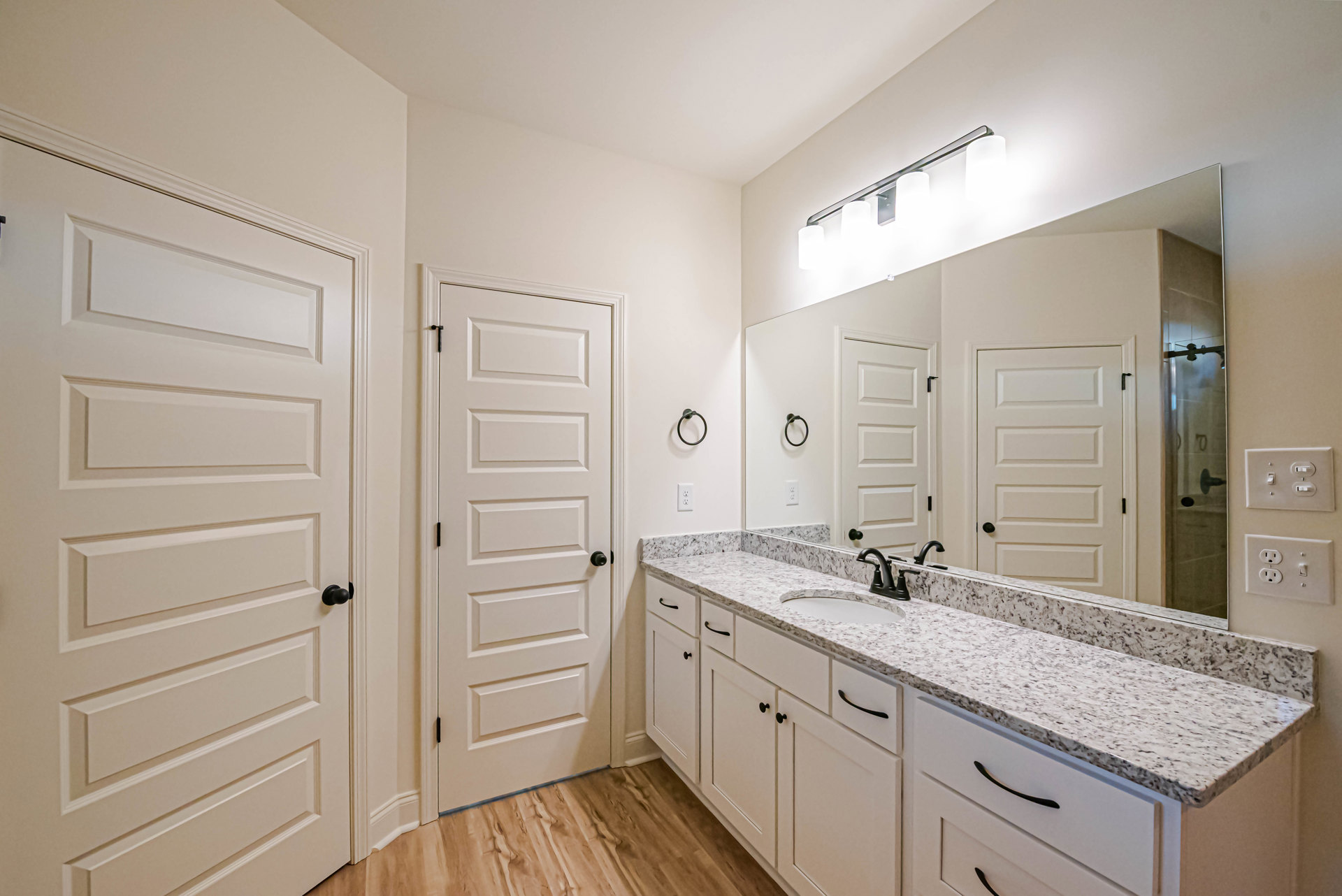 Bathroom with white cabinets, marble countertop, white doors featuring black knobs and handles, and a close-up of a wall switch