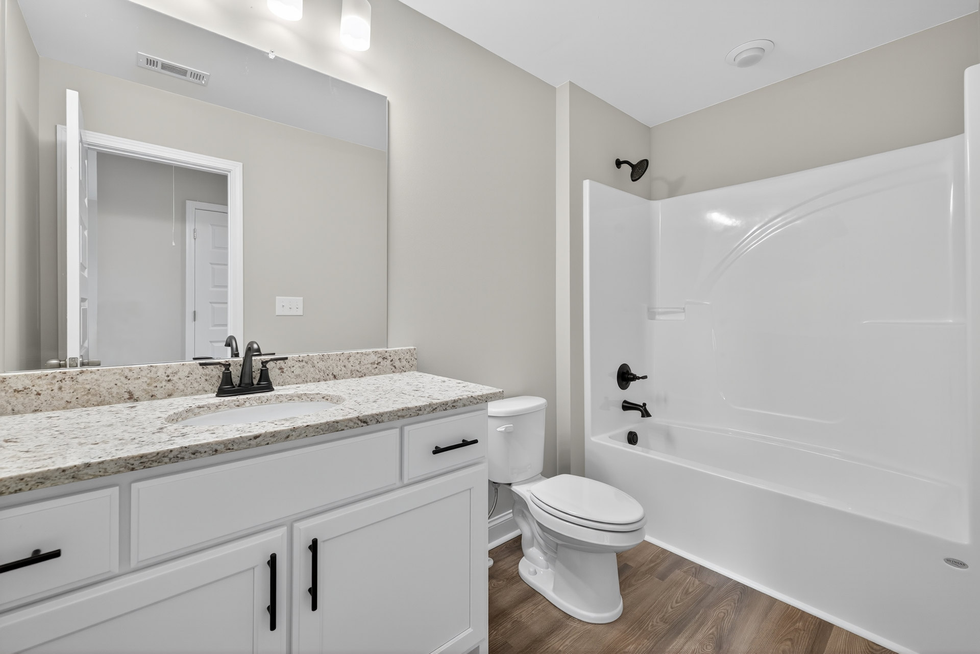 Modern bathroom featuring a freestanding white bathtub, white toilet, wall-mounted sink with matte black faucet, light gray tile walls, and minimalist cabinetry