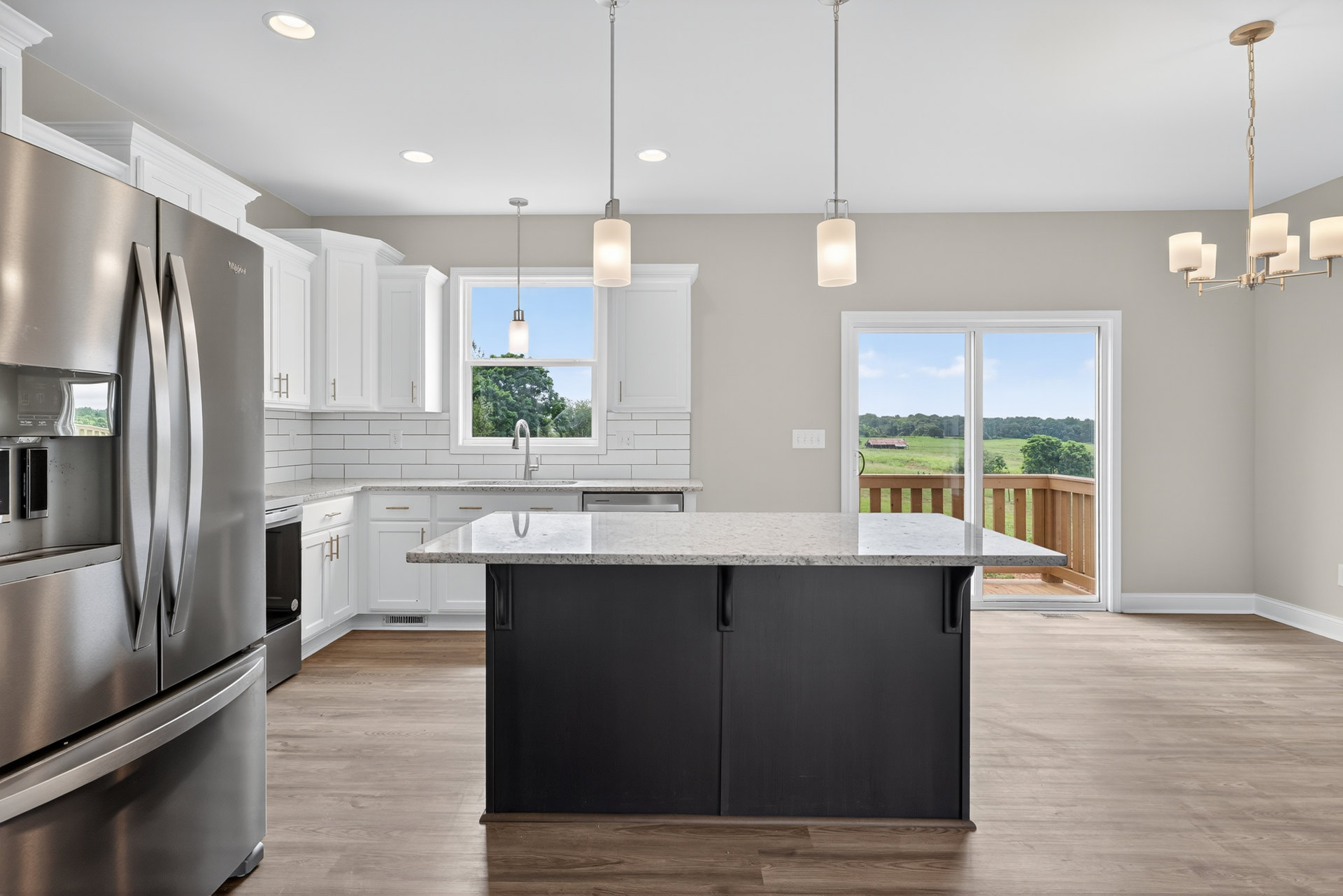 Spacious kitchen featuring a marble-topped island, white cabinetry, mirrored refrigerator side, modern white light fixture, and stainless steel sink