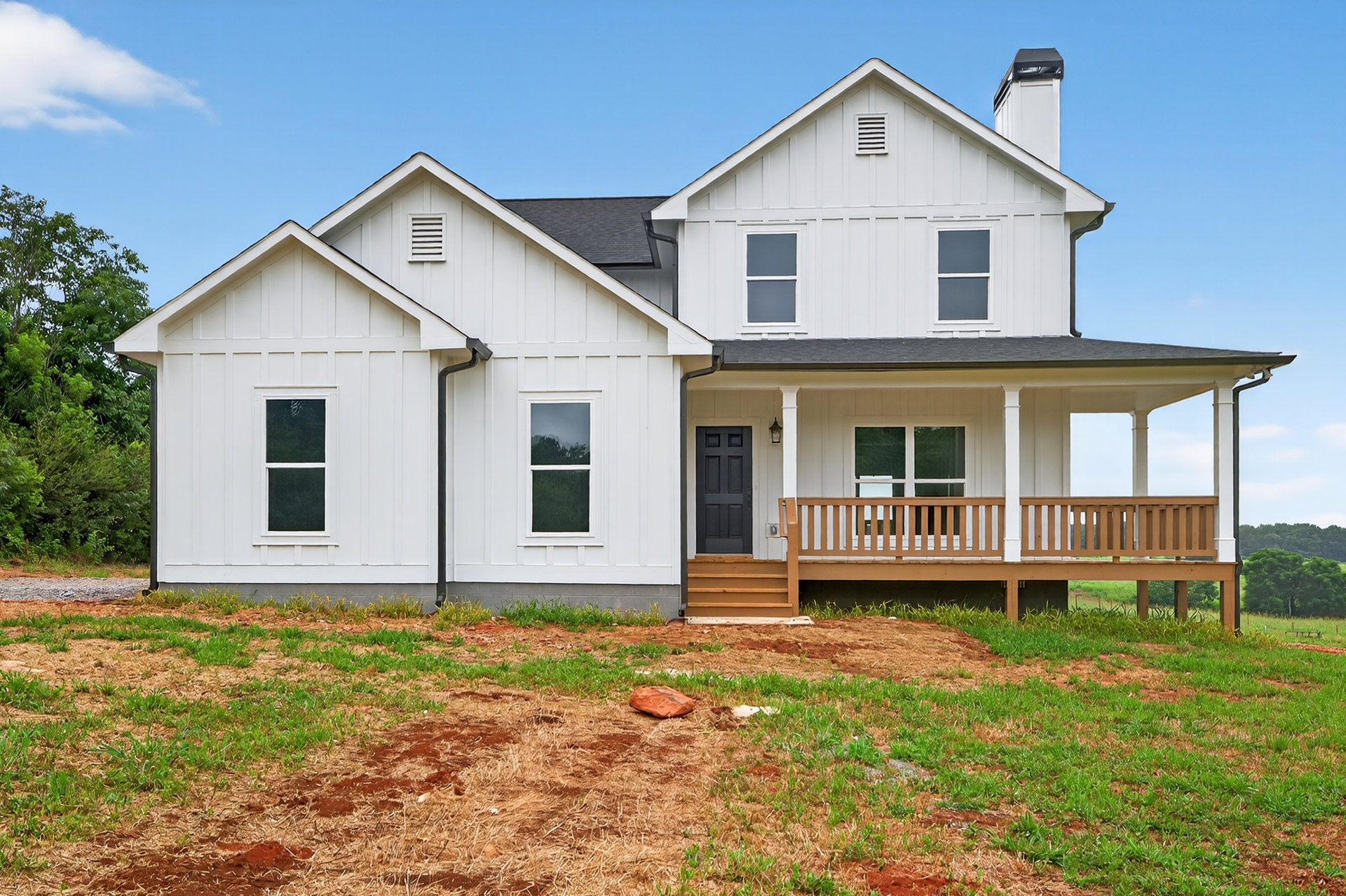 White house with wide front porch supported by white columns, manicured green lawn, white-framed windows, brown decorative object and rocks near entry.