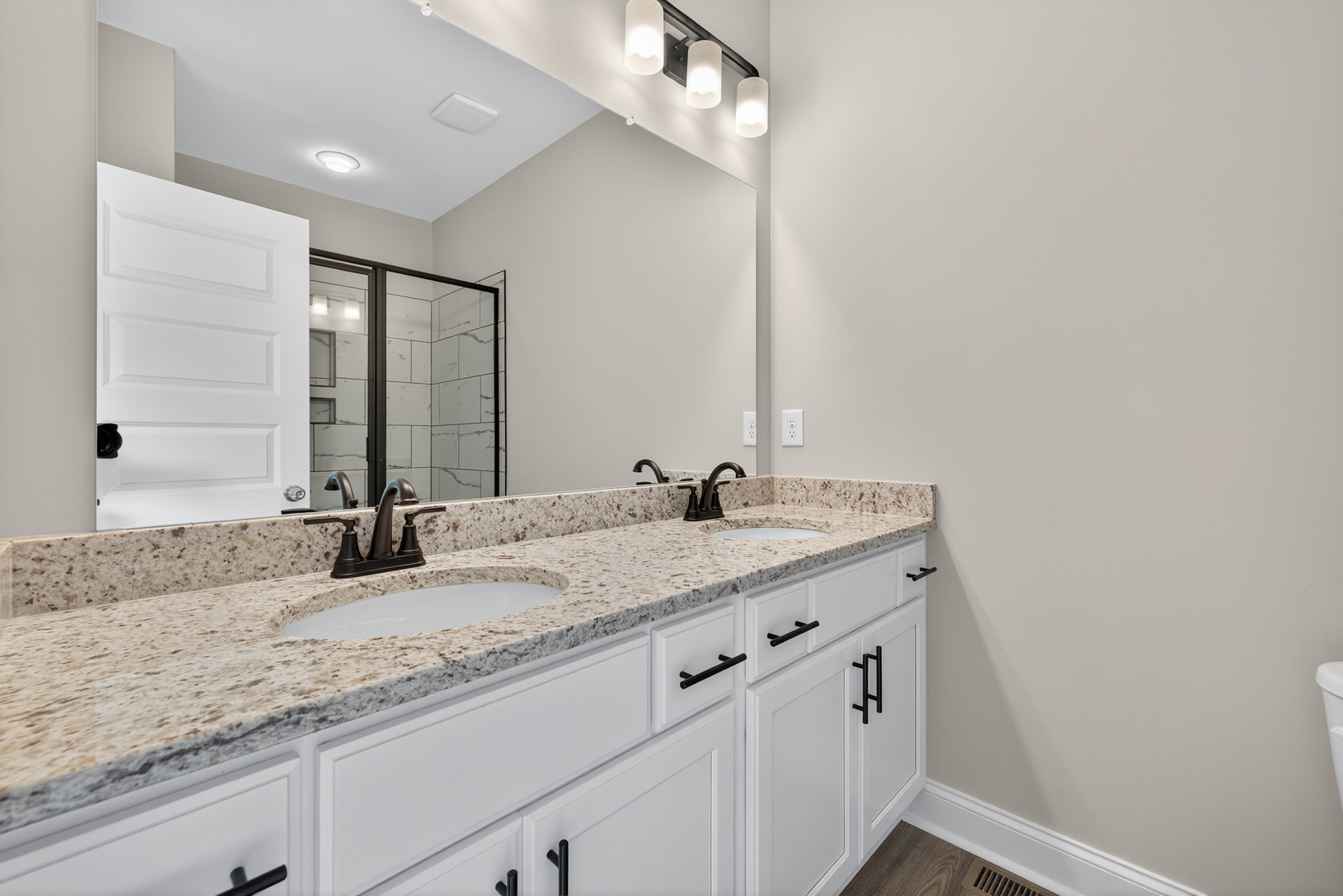 Bathroom featuring a marble countertop with undermount sink, large framed mirror, glass-enclosed shower, white cabinetry with black hardware, and recessed lighting.