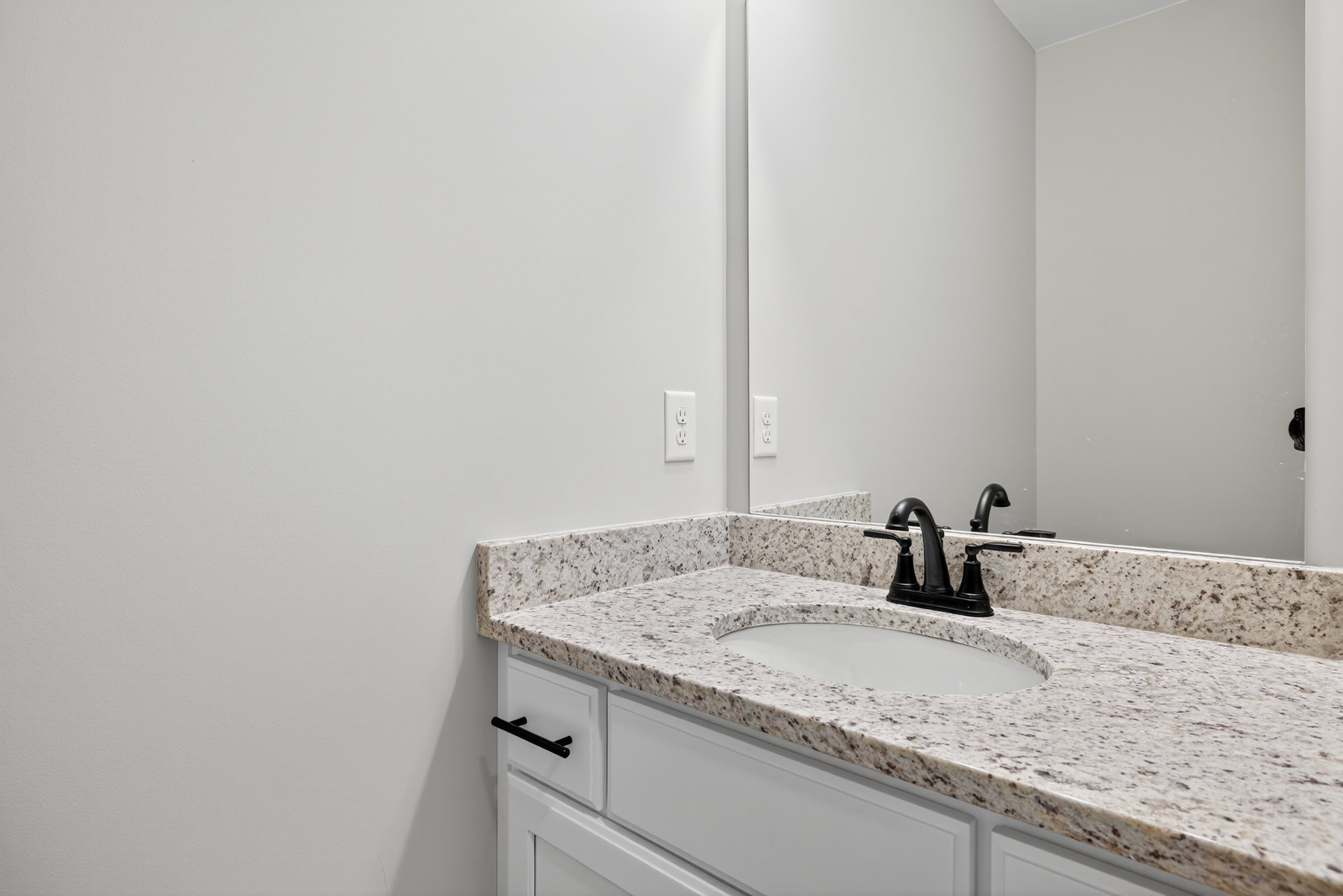 Marble countertop with black faucet and rectangular sink beneath a frameless mirror, white tile wall, minimalist bathroom design
