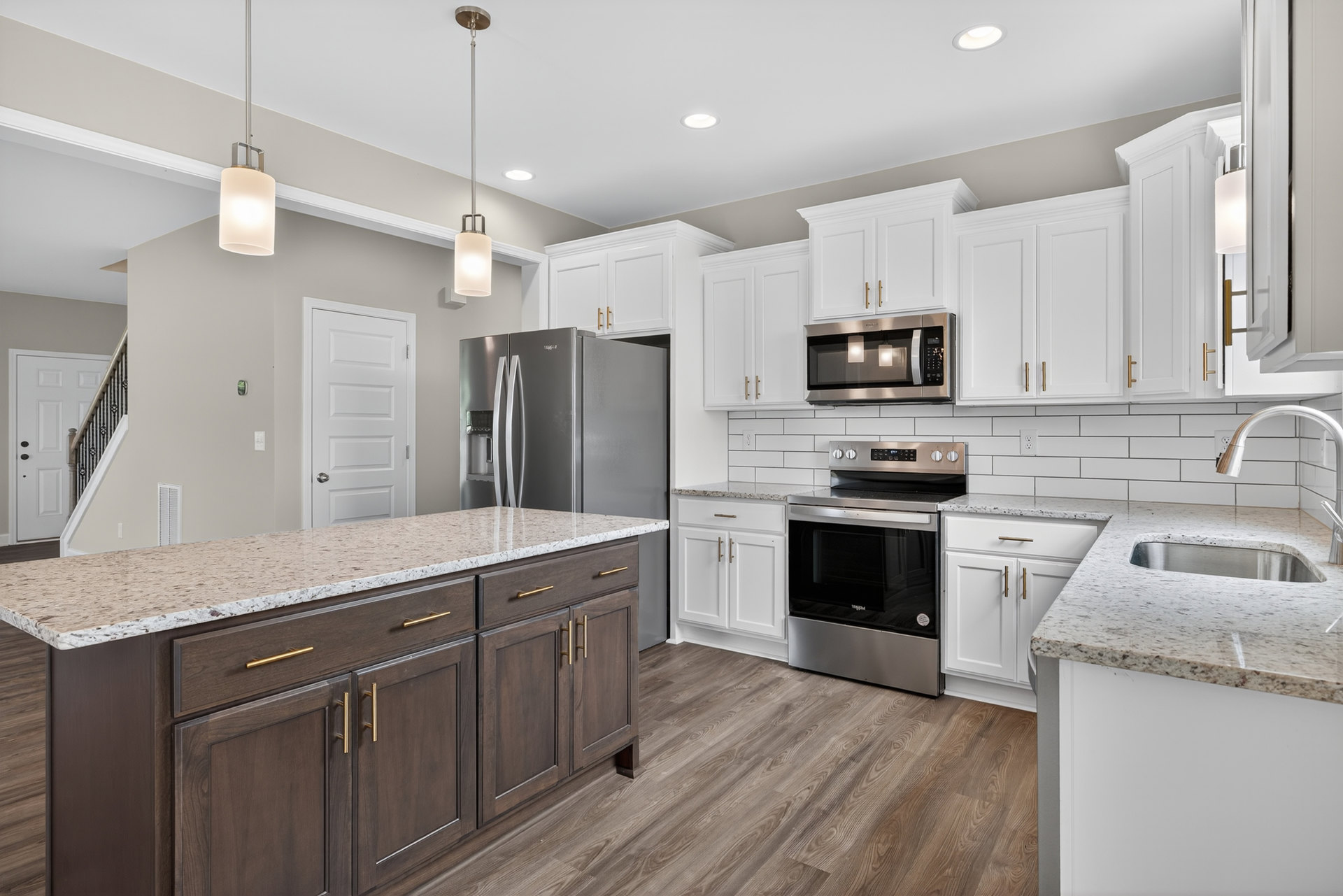 White kitchen with marble countertops, stainless steel stove with a pan, built-in microwave, kitchen island, white cabinetry, and a close-up of a white column.