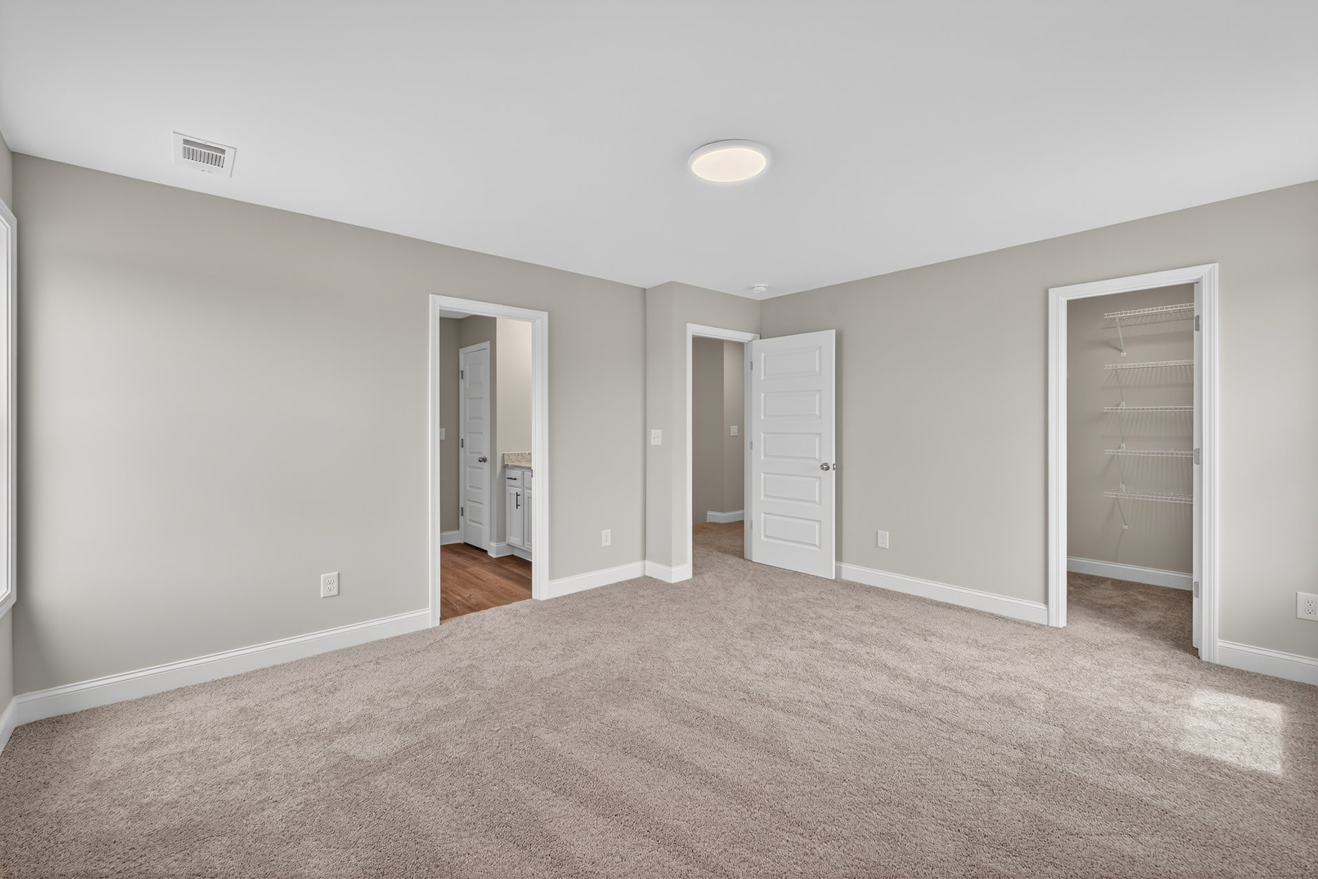 Beige carpeted floor, white walls, white door with silver handle, white ceiling, simple molding