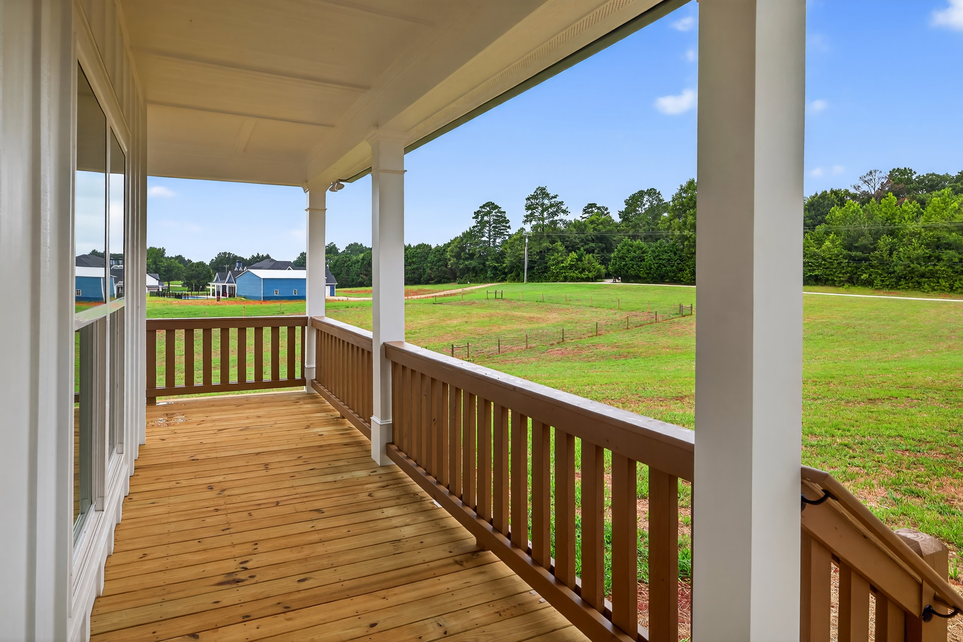 Wooden porch with white railings overlooking grassy field and trees, blue exterior siding, white roof, and windows visible.