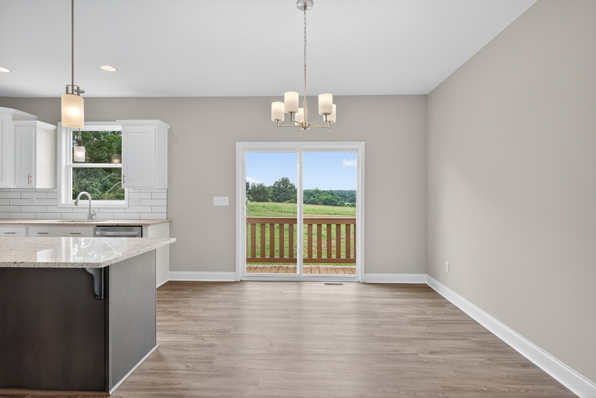 Kitchen with marble island, white cabinetry, wood flooring, sliding glass door opening to deck and field, pendant light fixture hanging from chain