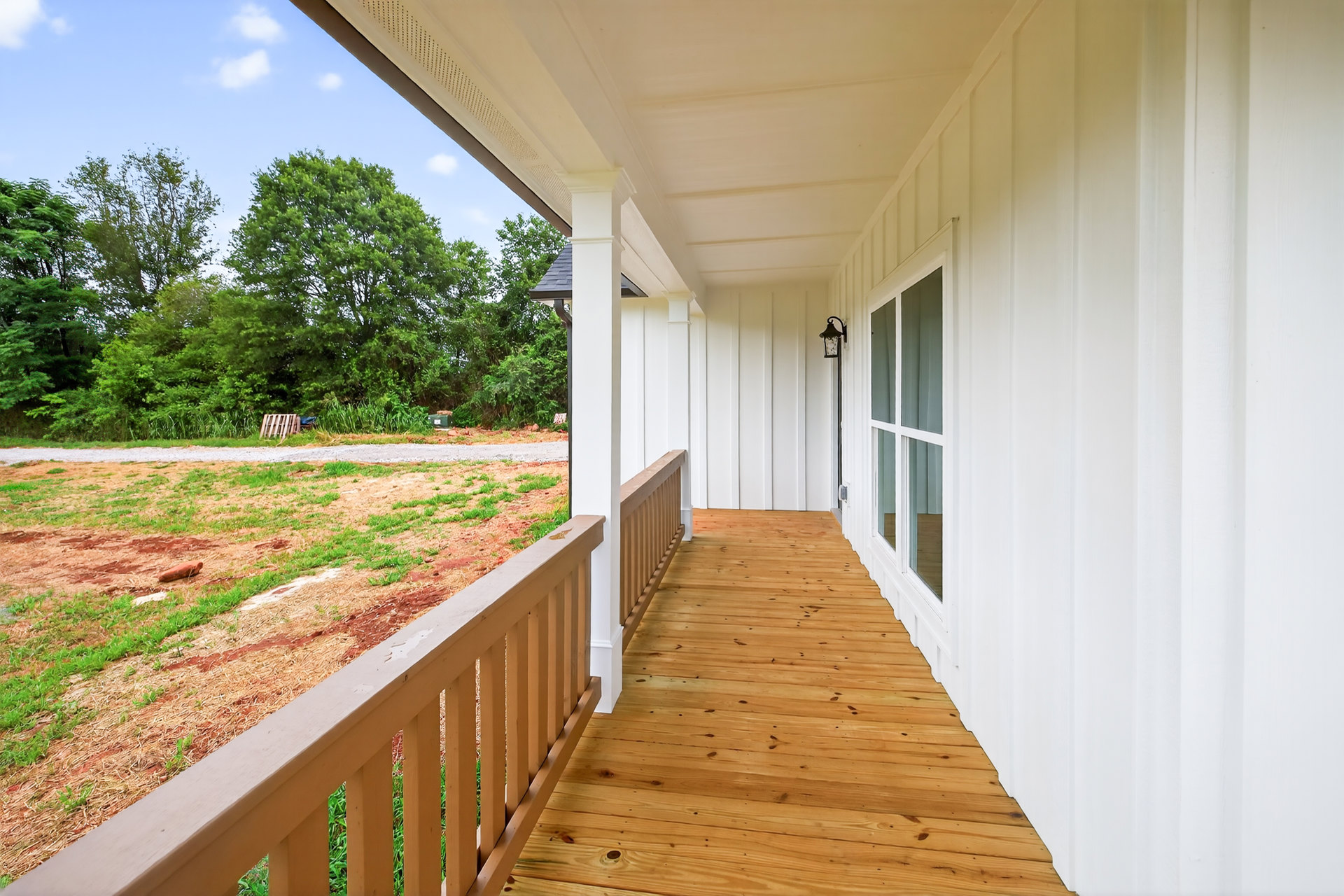Wood porch with white railings, wooden deck floor, and fenced grassy yard beside a white house.