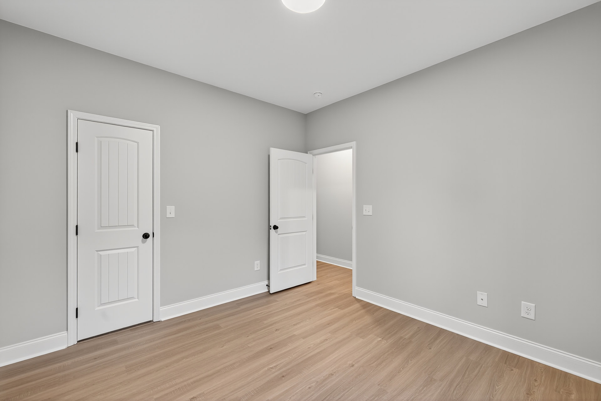 White paneled door with black knob, wood plank flooring, white walls with electrical outlets, black trim molding