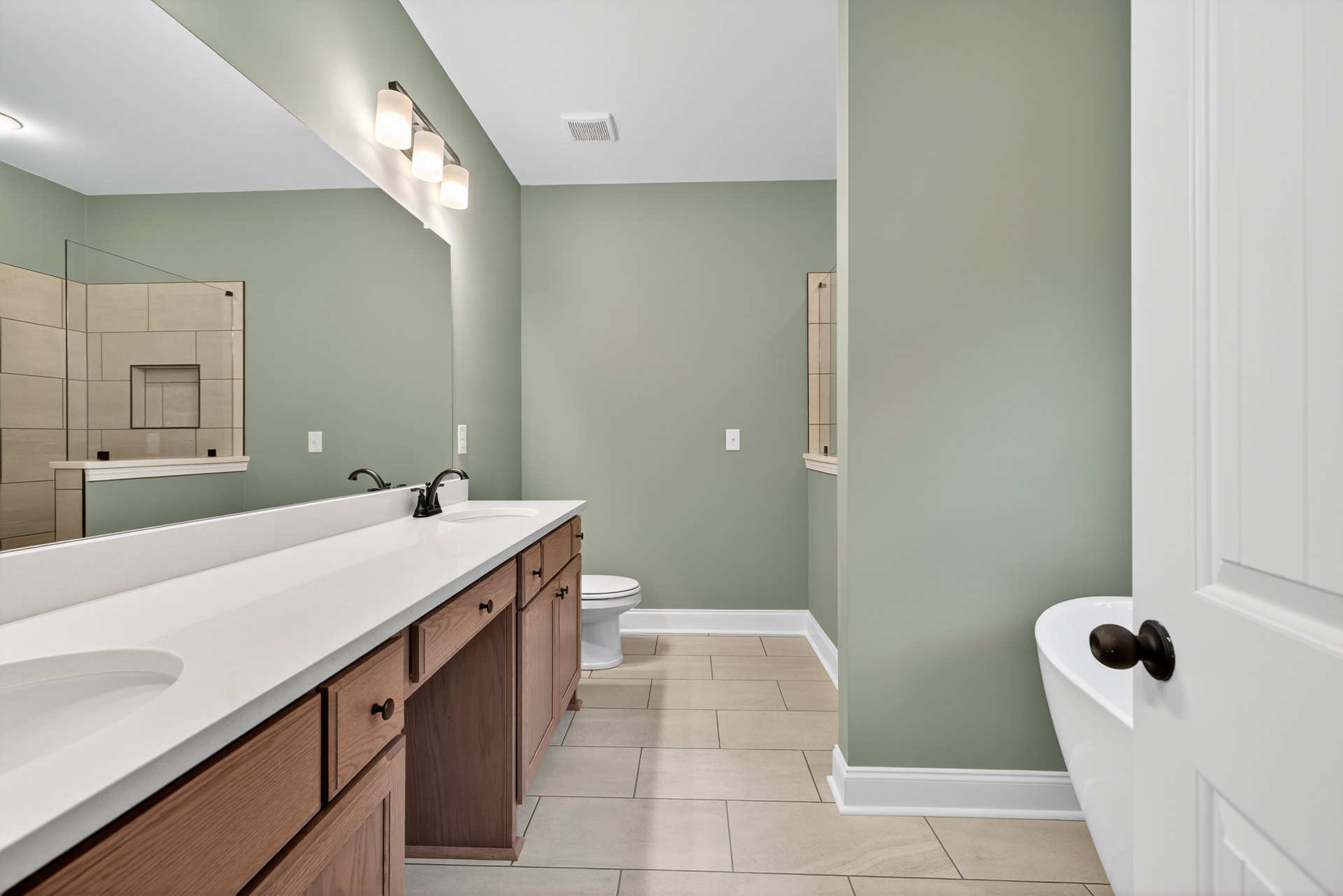 Bathroom with freestanding tub, double sinks set in wooden cabinetry, white tile walls, and chrome plumbing fixtures