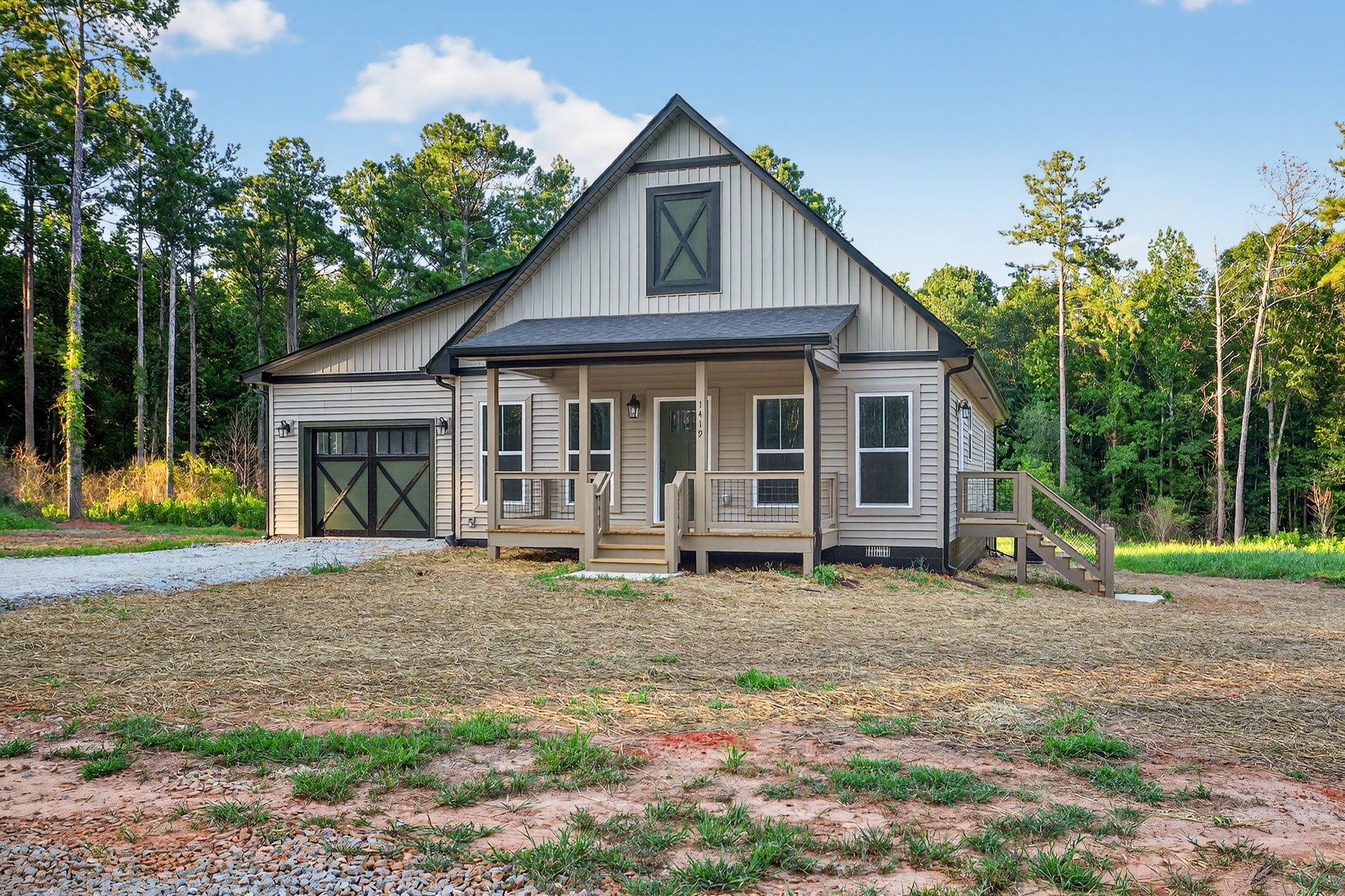 Two-story house with green garage door, black trim, wooden stairs, covered porch, and grass lawn under partly cloudy sky